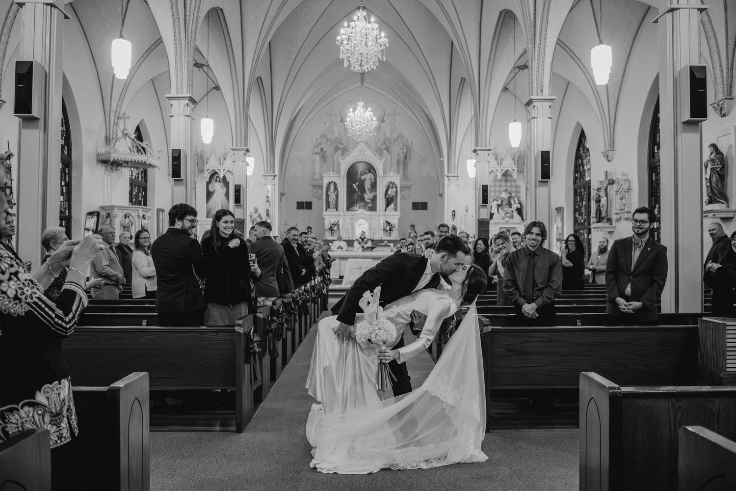A black and white image of a wedding ceremony taking place in a grand, ornate church interior.