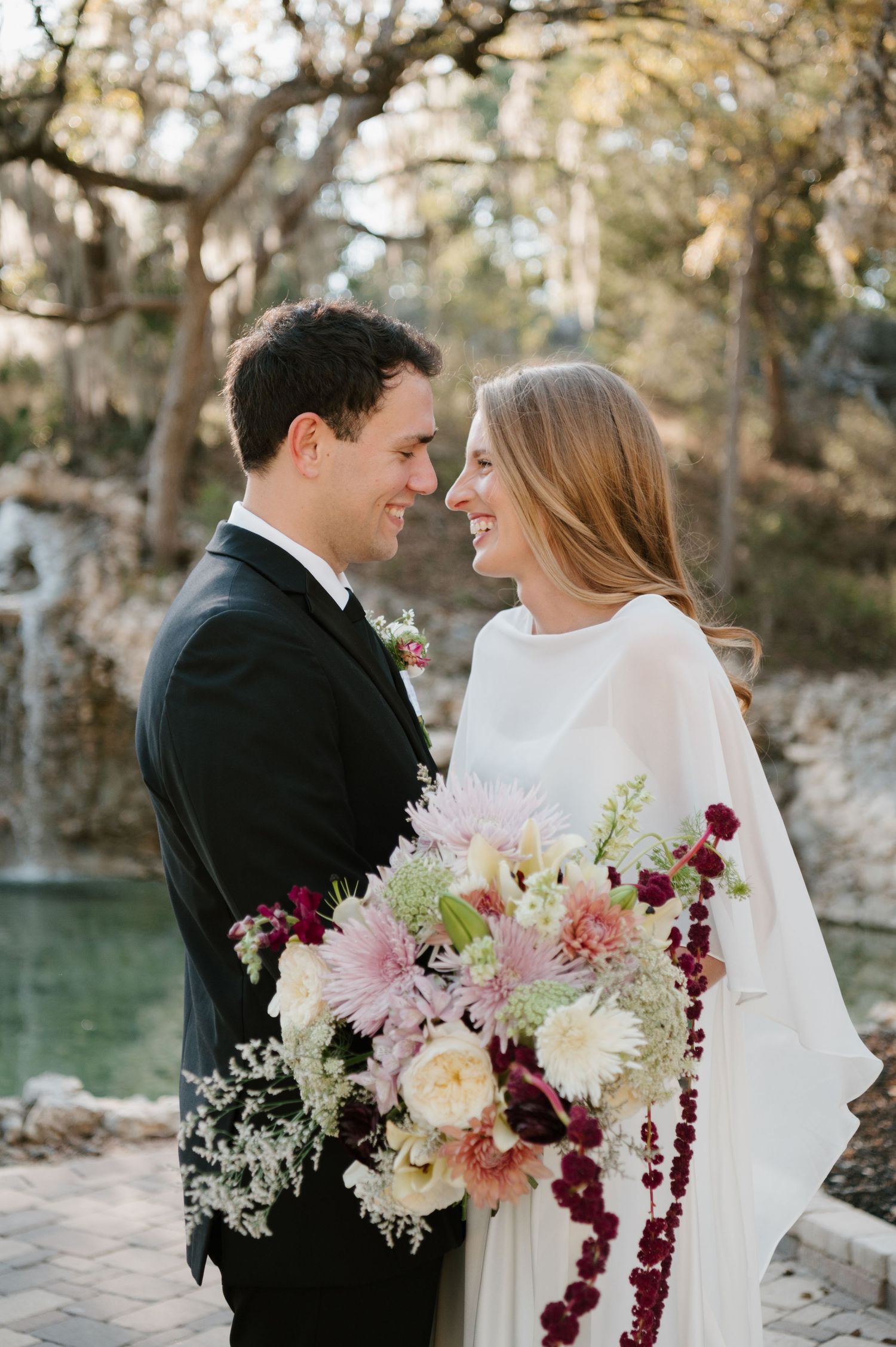 Romantic wedding portraits with burgundy floral bouquet against natural stone backdrop.