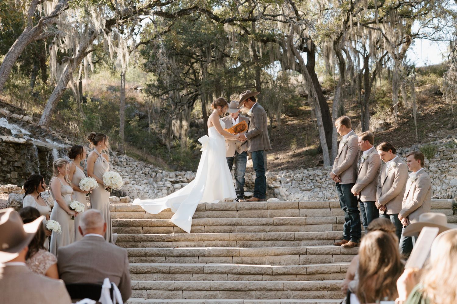 Wedding ceremony taking place on stone steps surrounded by trees and natural scenery.
