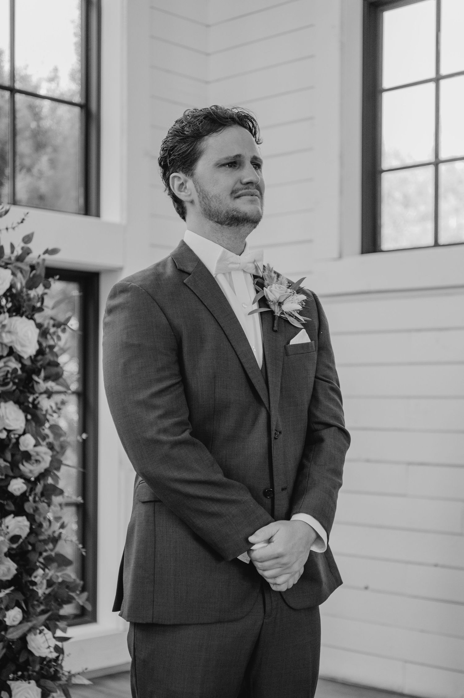 Black and white photo showing groom in dark suit with boutonniere waiting anxiously at a white chapel venue.