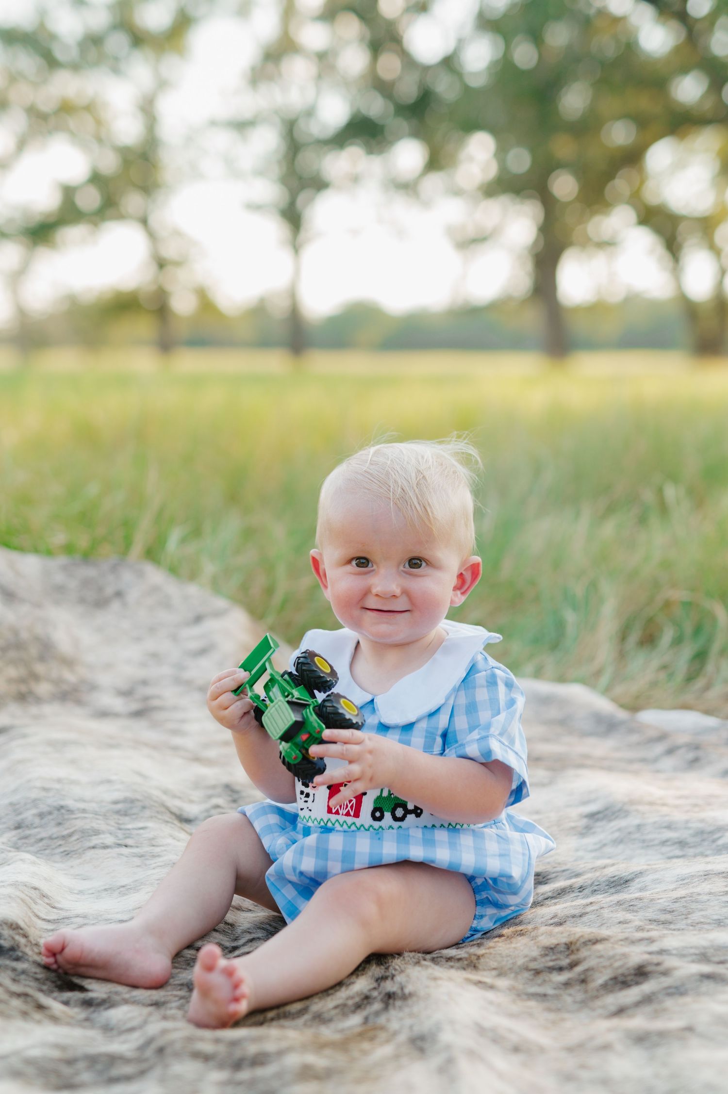 A baby in blue gingham romper plays with a green toy while sitting on sandy ground in a series of photos.