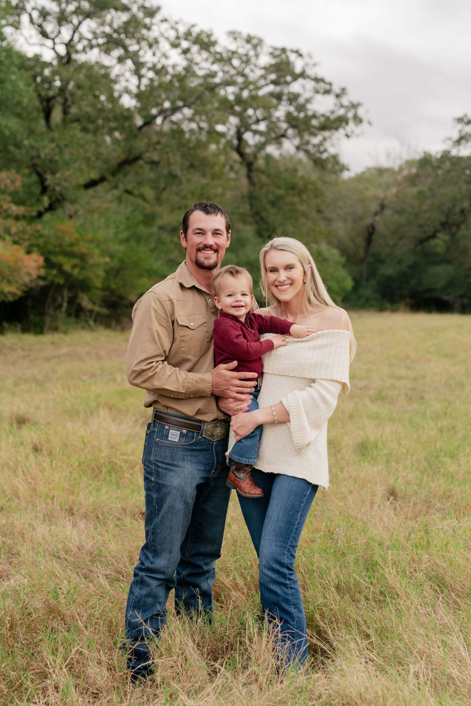 A young family poses together in a field with fall foliage in the background.