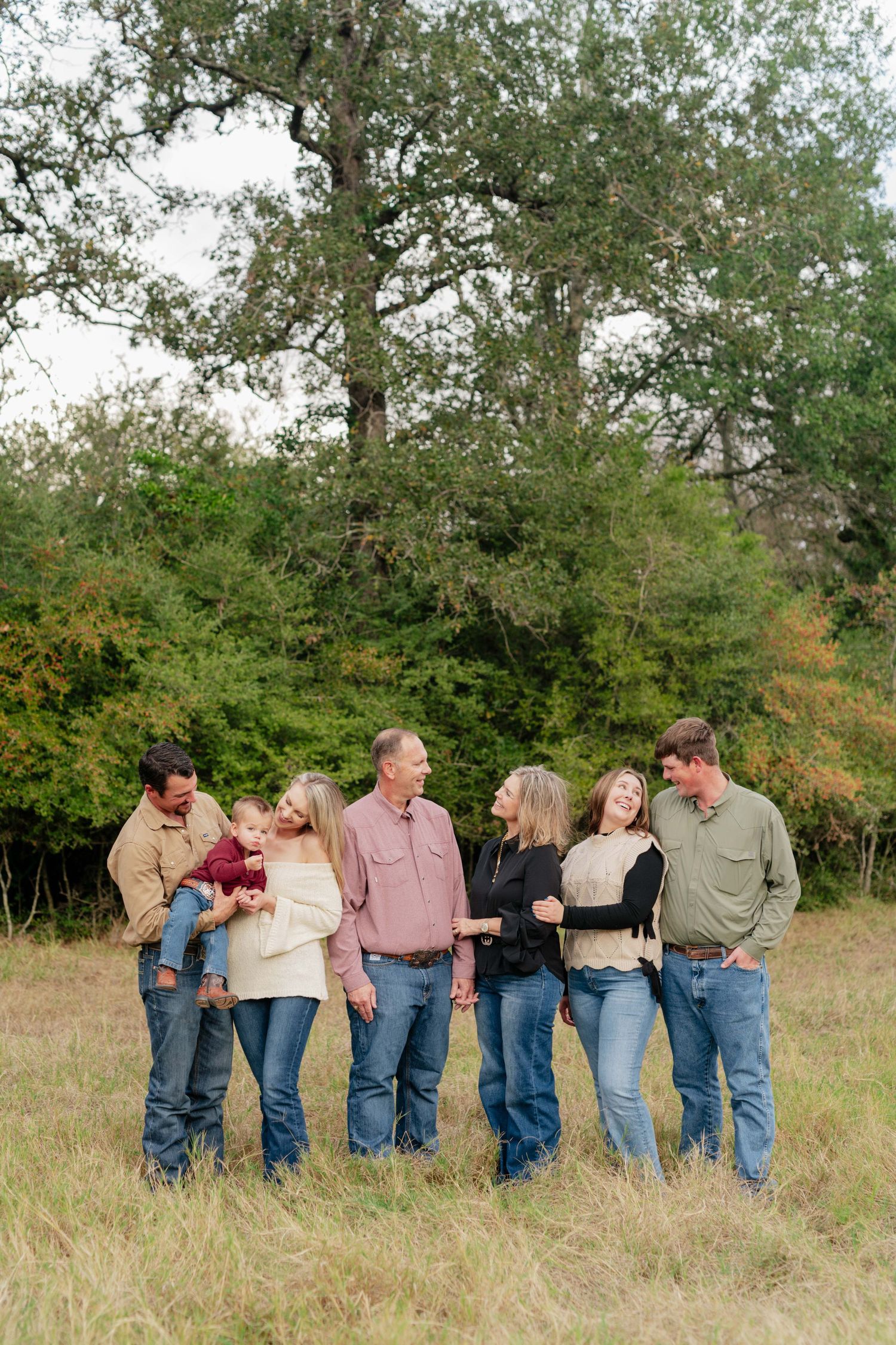 Group of six people in casual attire standing close together in a field with trees behind them.