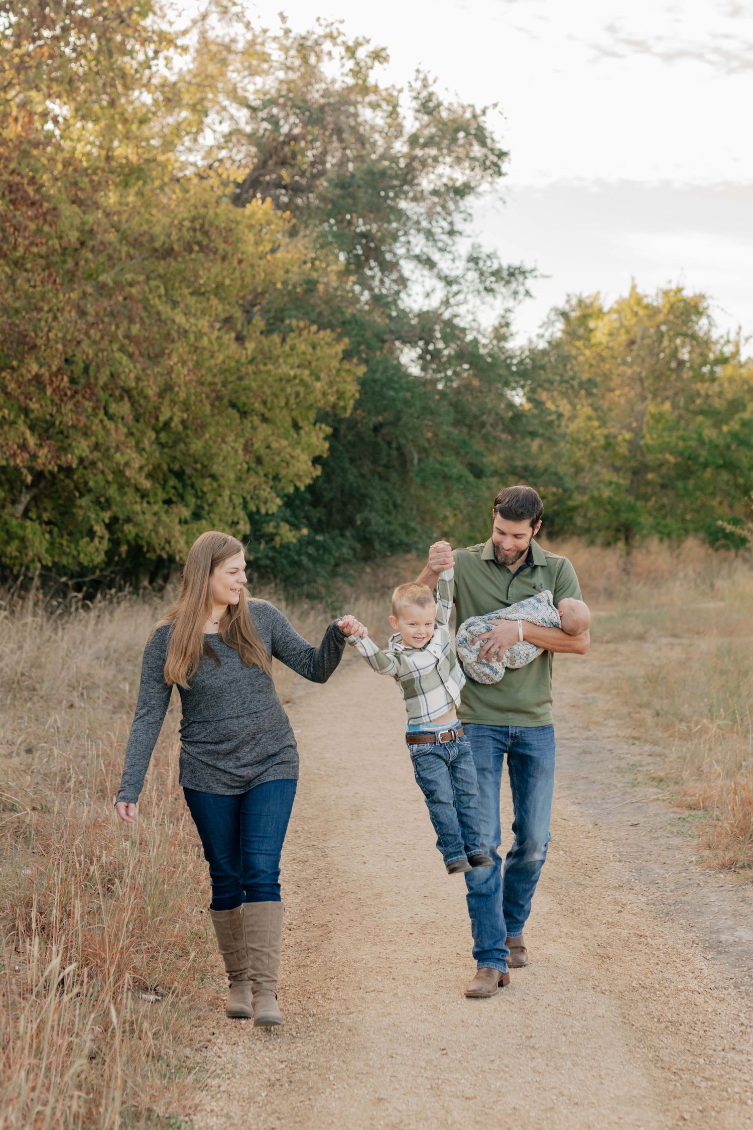 Family enjoying a playful moment on a dirt path surrounded by fall foliage.