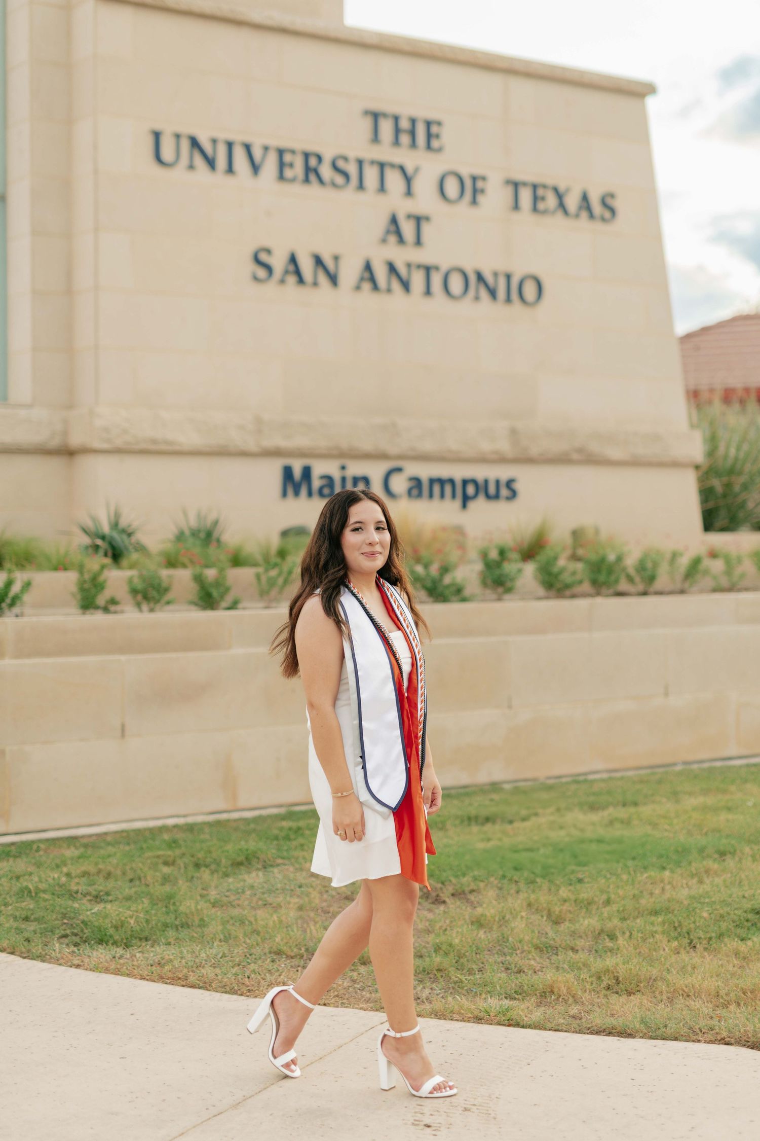 Graduate poses at University of Texas at San Antonio main campus sign.