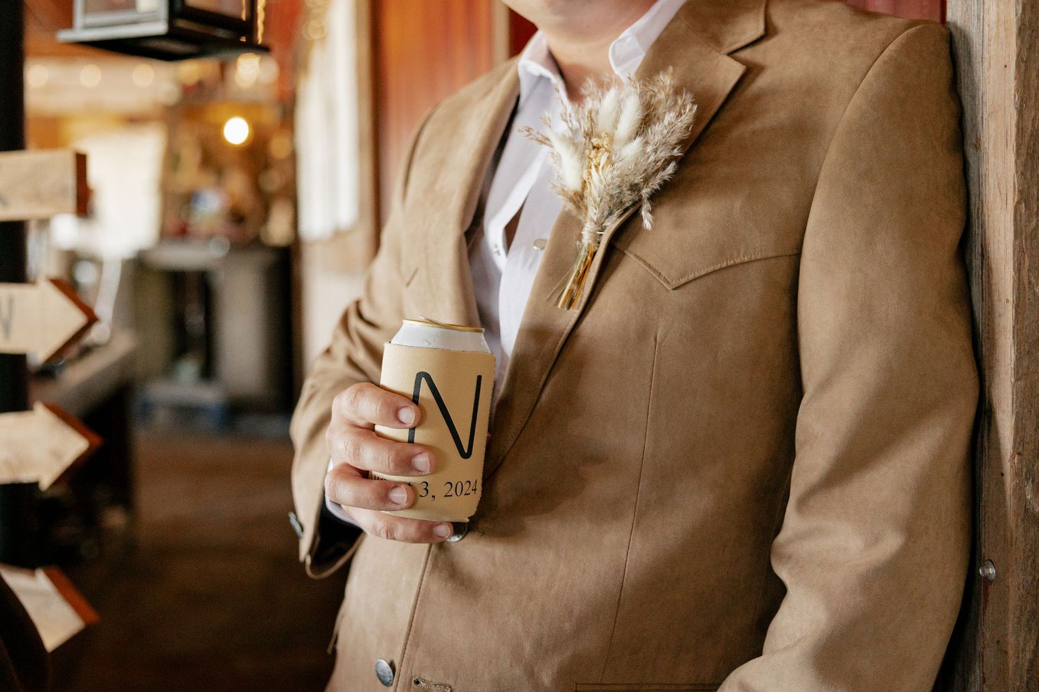 Person in tan suit vest holding a beverage at an indoor venue.