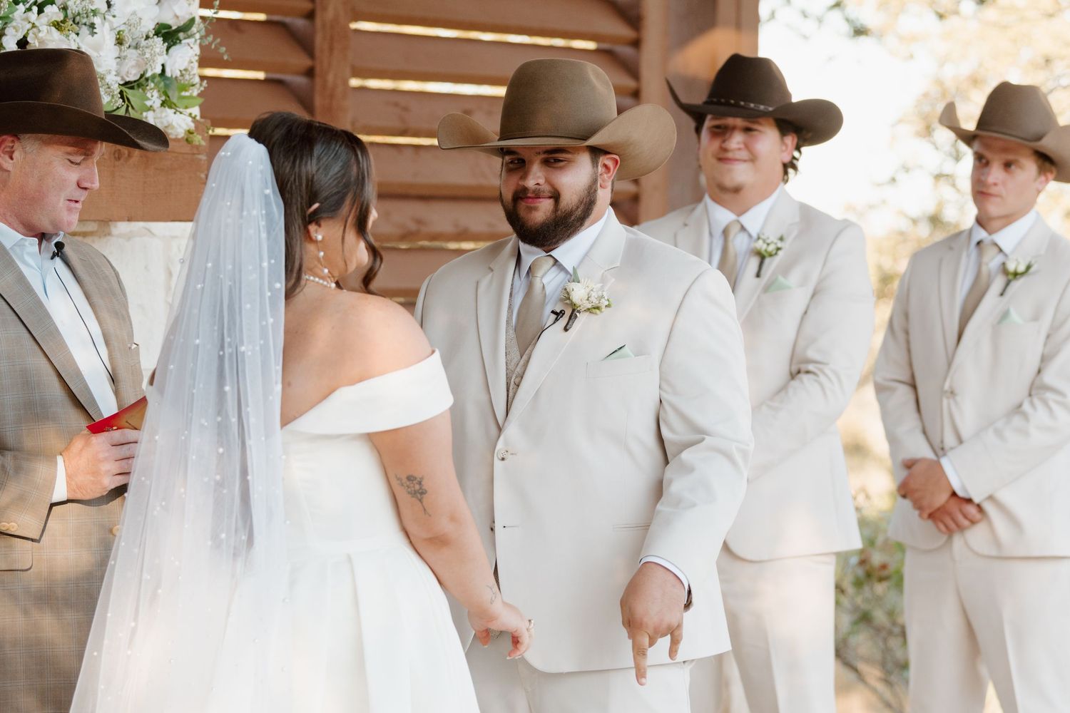 Wedding party in light beige suits and cowboy hats stands at rustic outdoor ceremony.