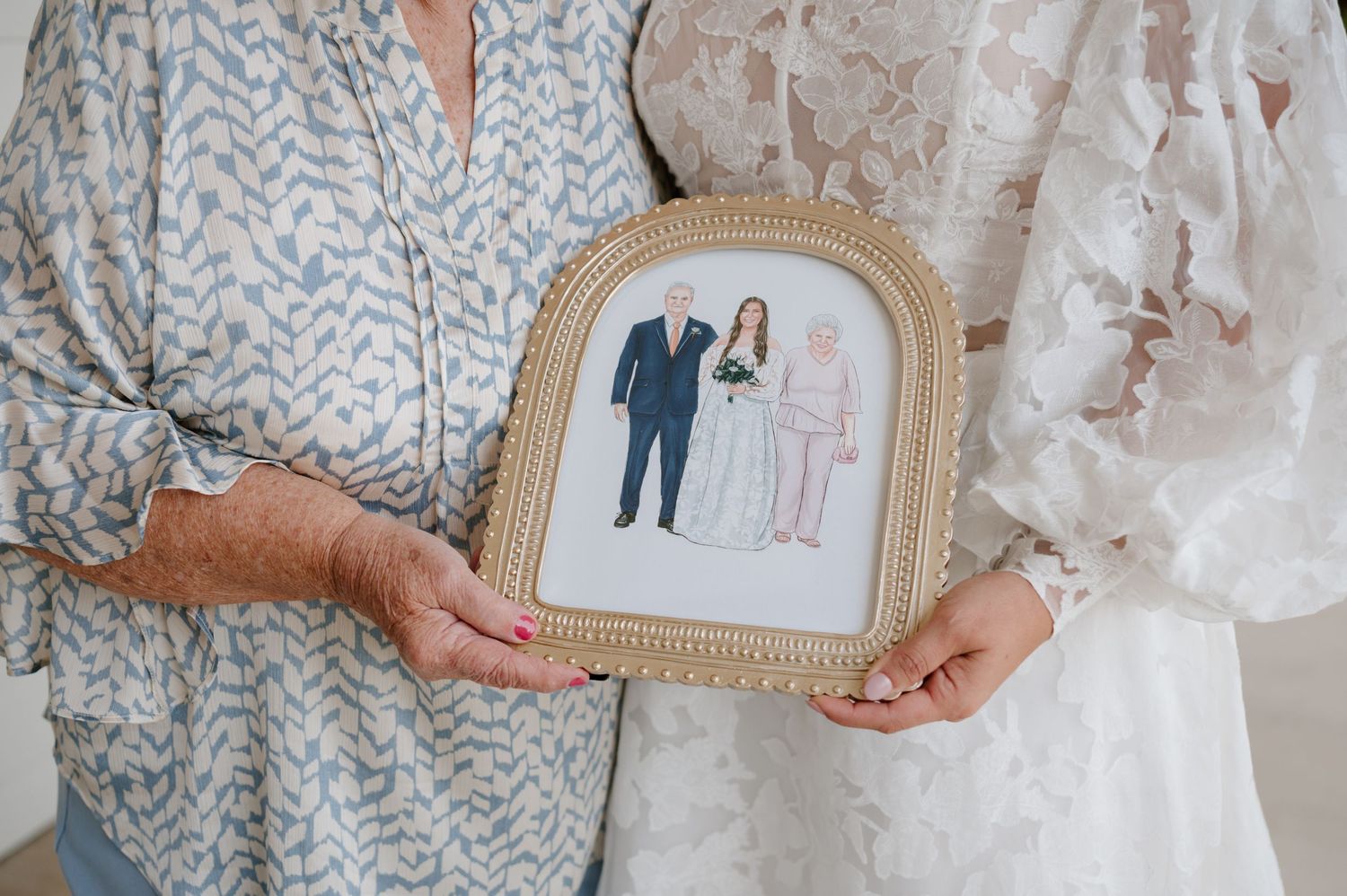 Hands holding a delicate gold-framed illustrated portrait at a wedding venue.