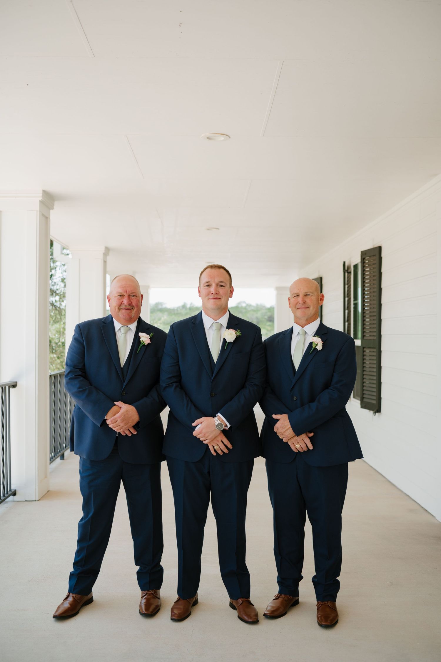 Small group of groomsmen in navy suits posing on white porch.