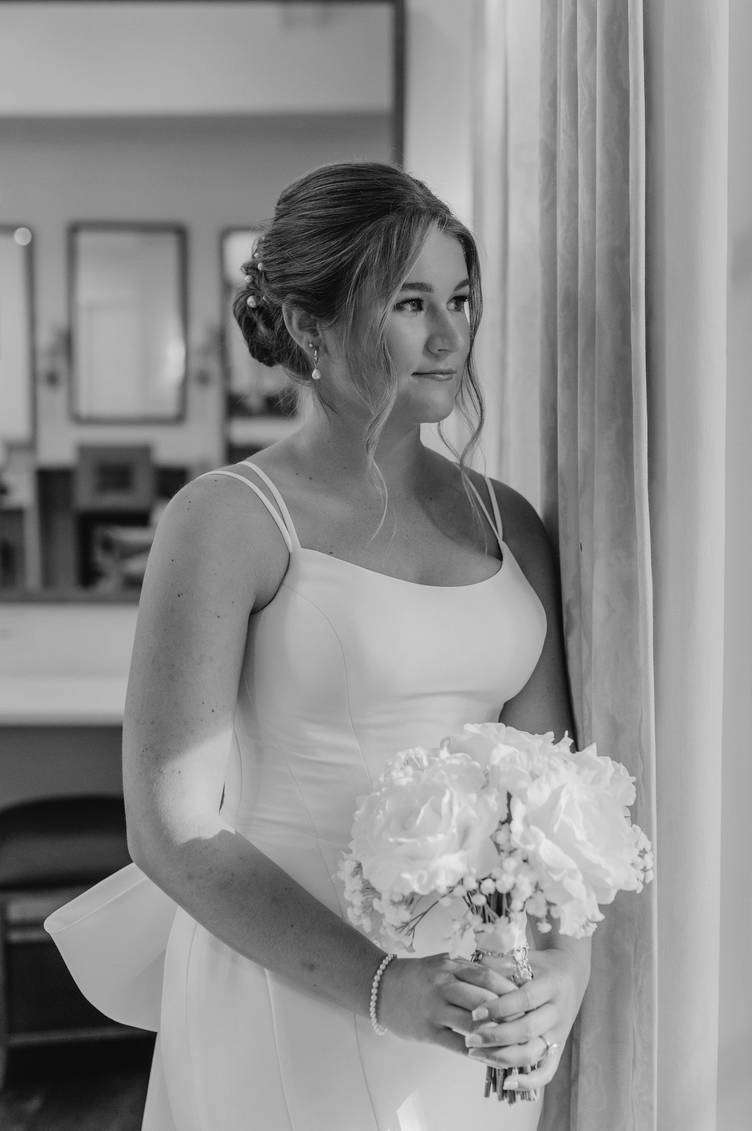 Black and white portrait of bride holding bouquet in elegant indoor setting.