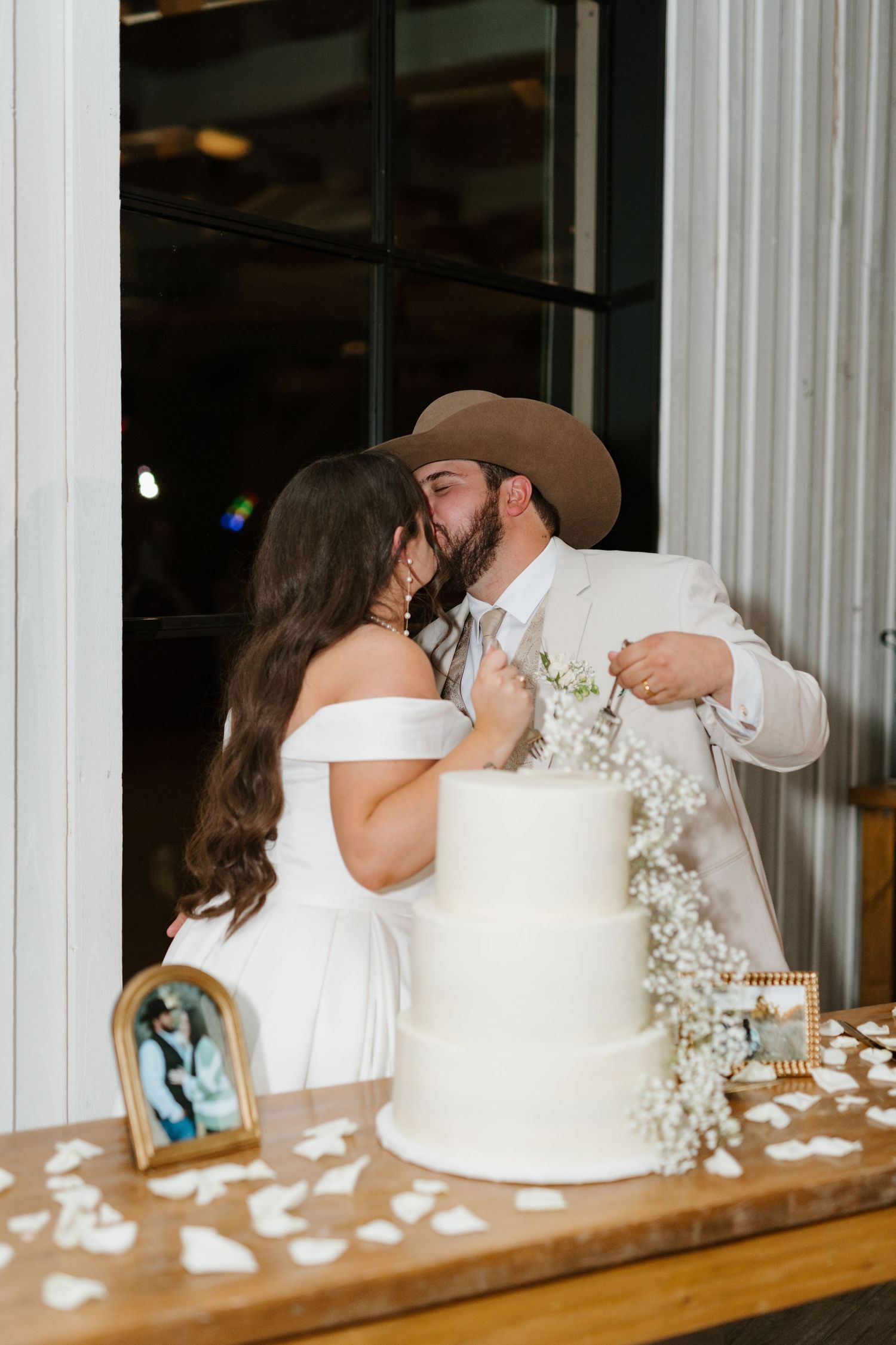 A bride and groom share a romantic moment beside their elegant white wedding cake decorated with baby's breath flowers.