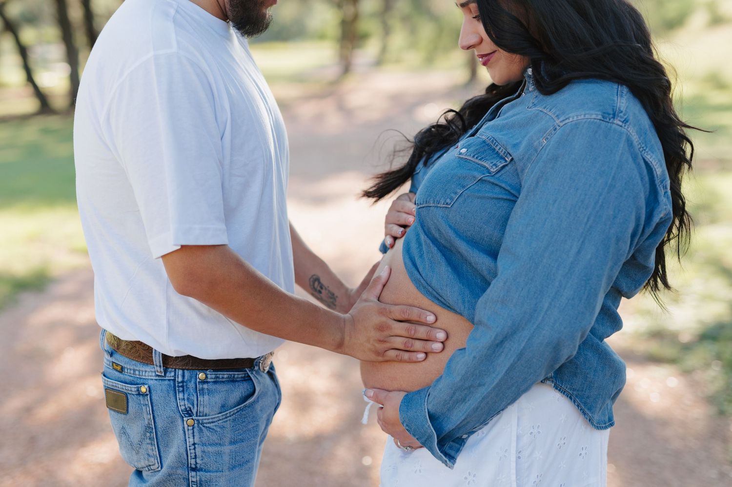 Couple in casual denim and white outfits embrace outdoors during a romantic engagement photo session.