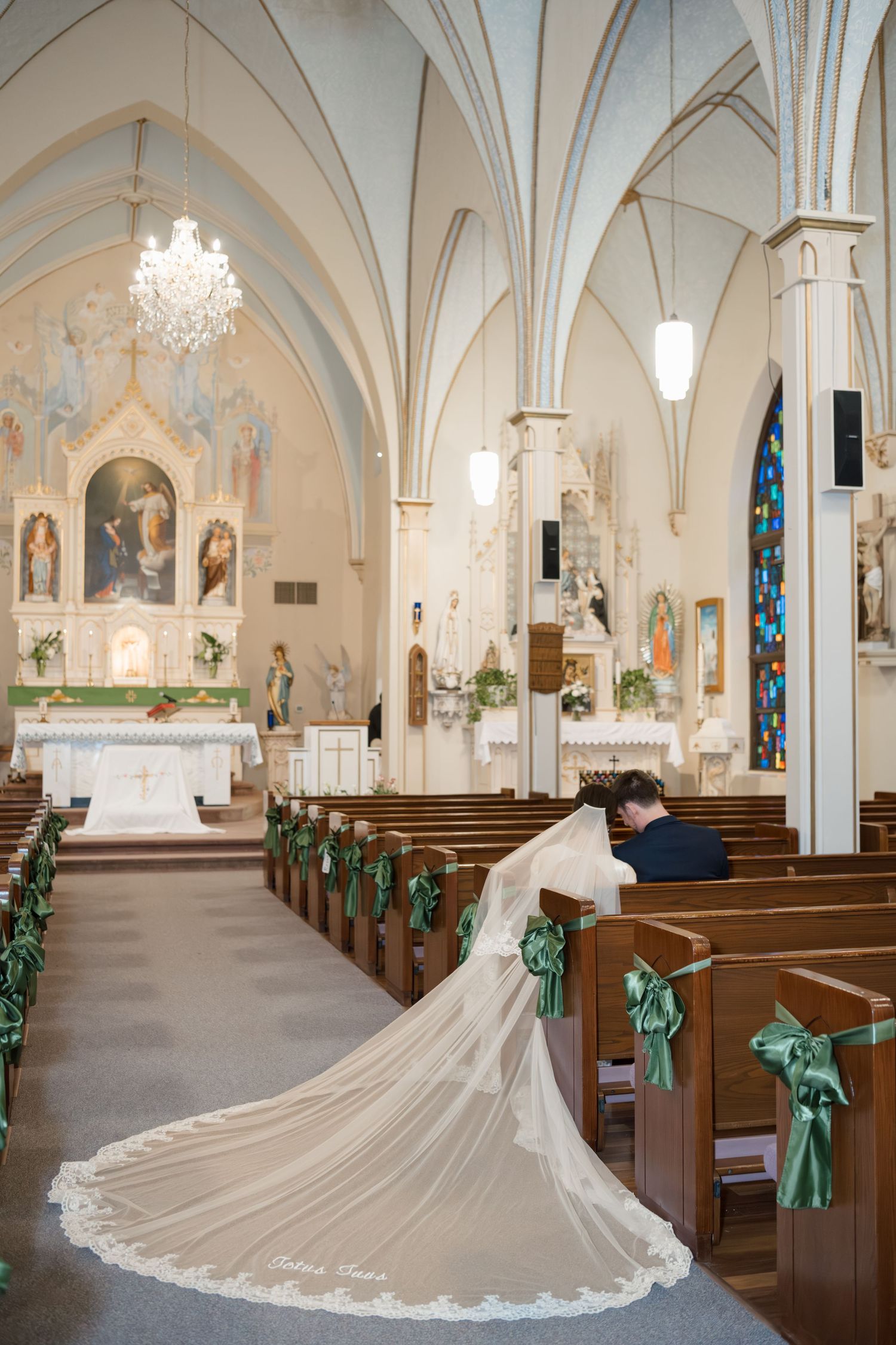 A stunning cathedral interior with vaulted ceilings, wooden pews, and a long flowing white wedding veil trailing down the aisle.