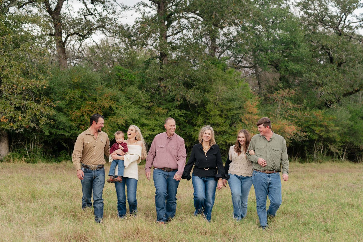 Group walking together in sync across an open field with trees and greenery in the background.