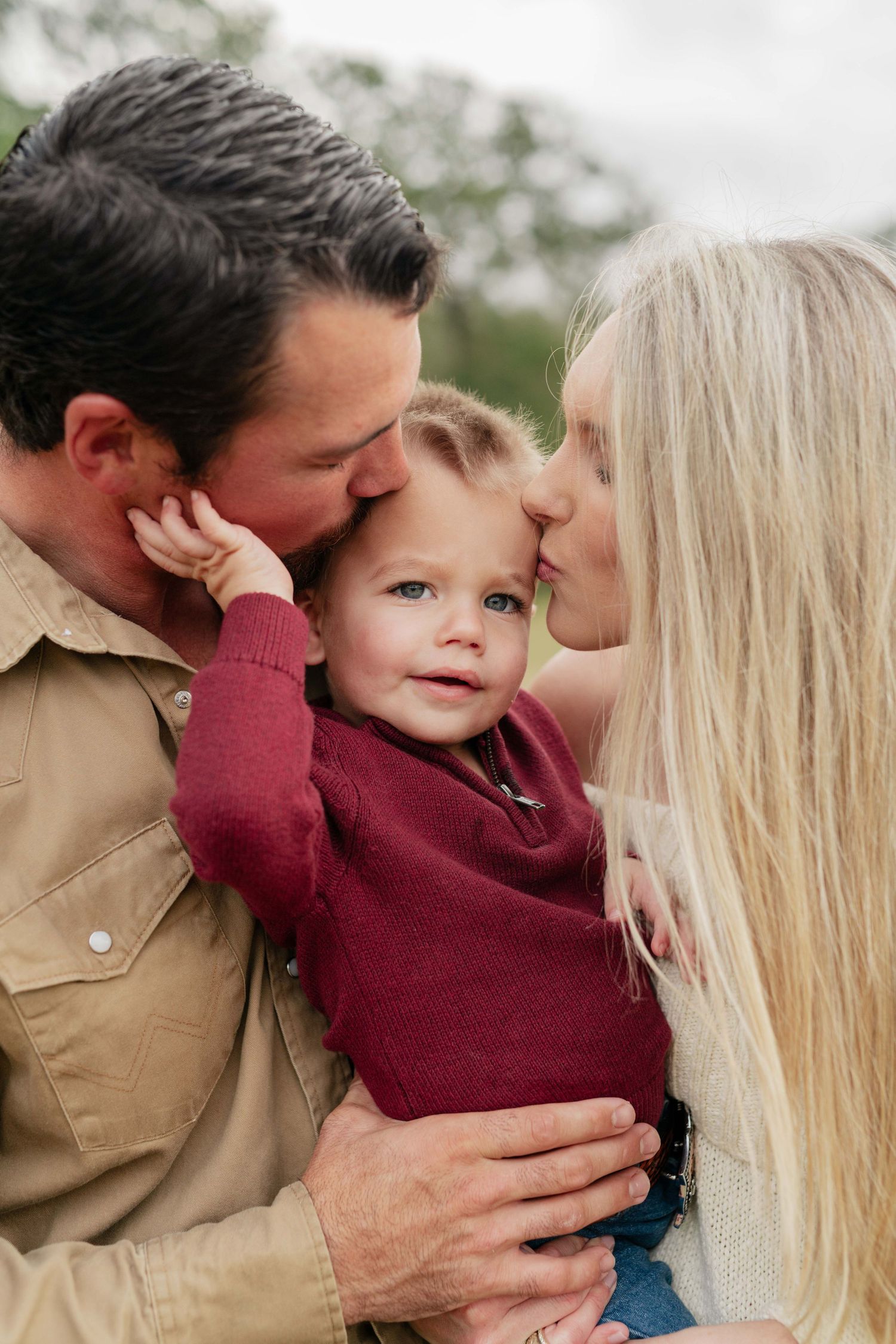 A loving family shares an intimate moment outdoors with their young toddler.