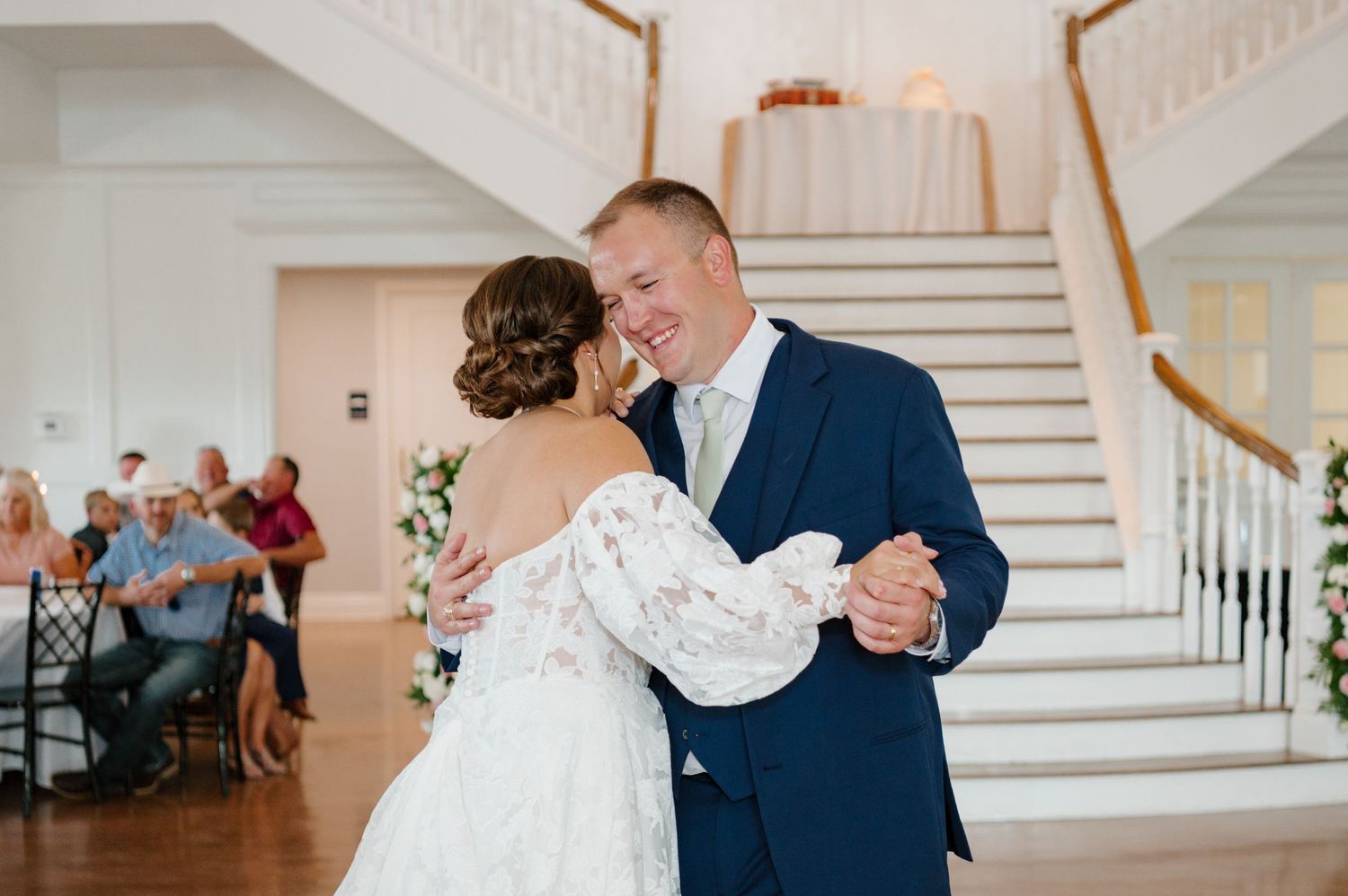 Intimate wedding dance moments captured in an elegant white reception venue with staircase.