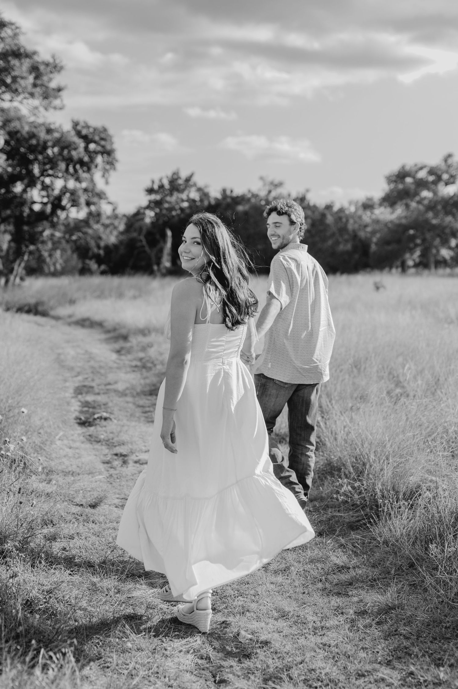 A couple walks along a scenic dirt path through tall grass in black and white photography.