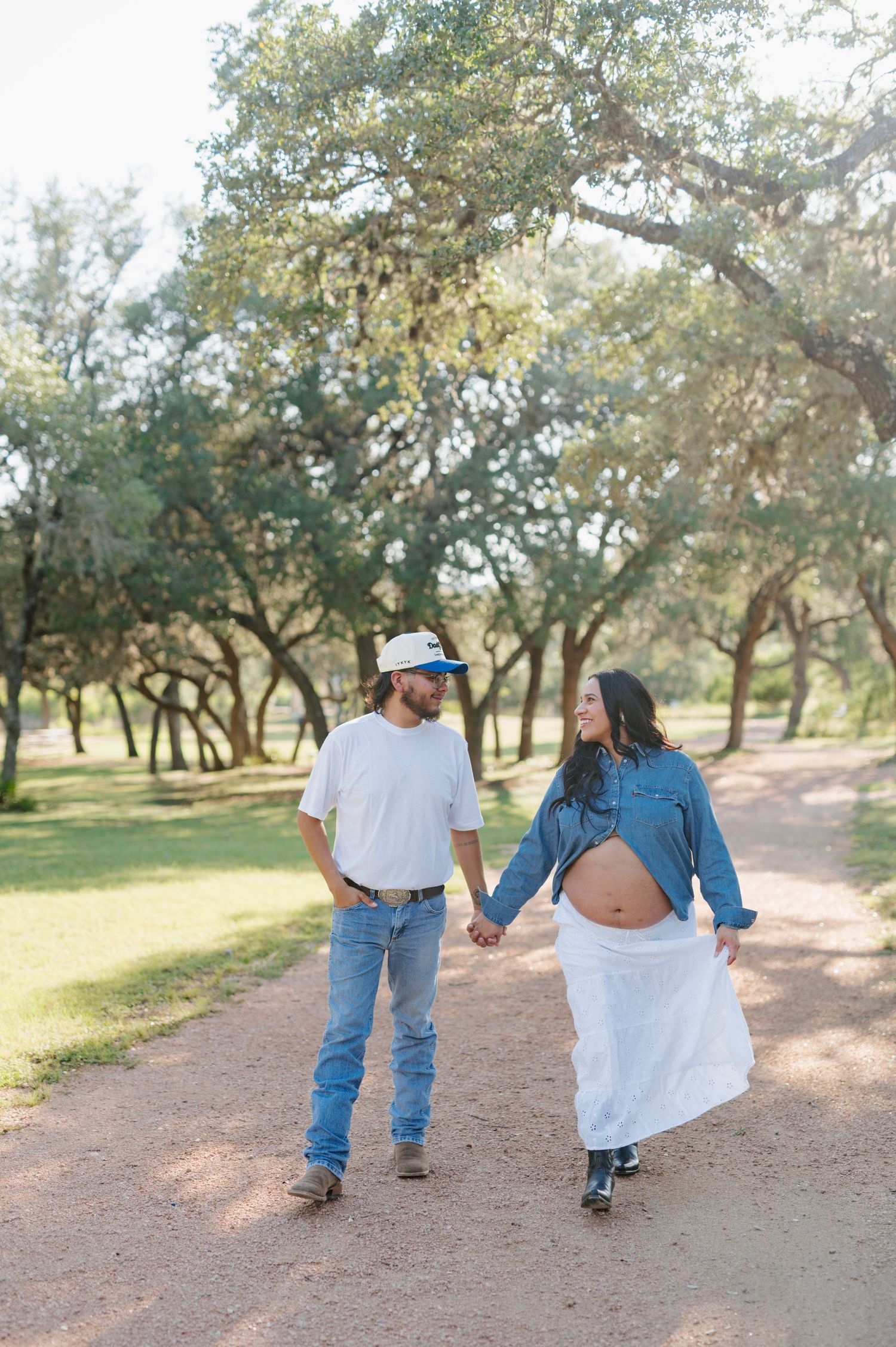 Couple walking together on a dirt path surrounded by oak trees in a natural outdoor setting.
