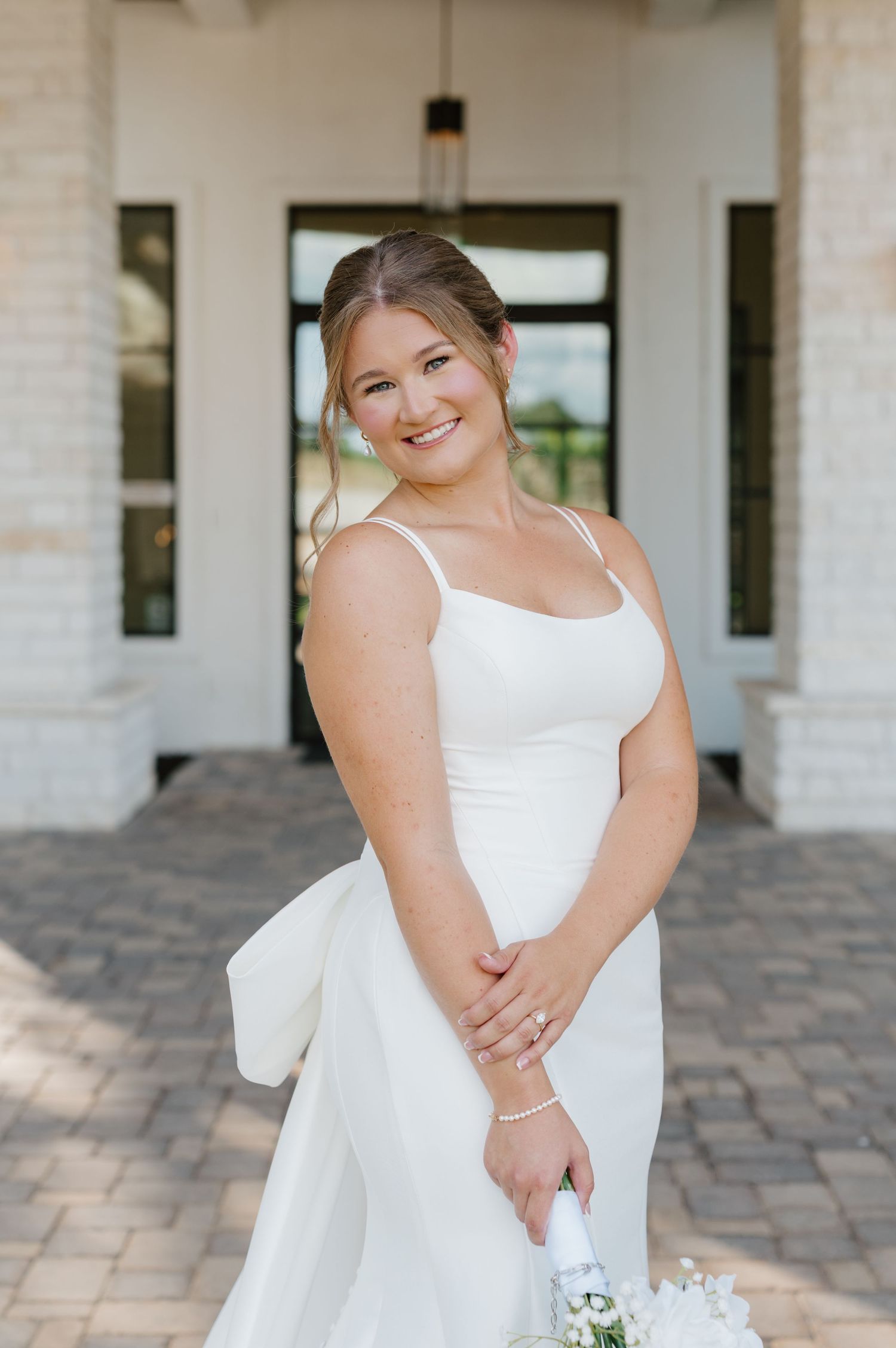 A bride in a classic white wedding dress poses elegantly on a stone patio with white columns in the background.