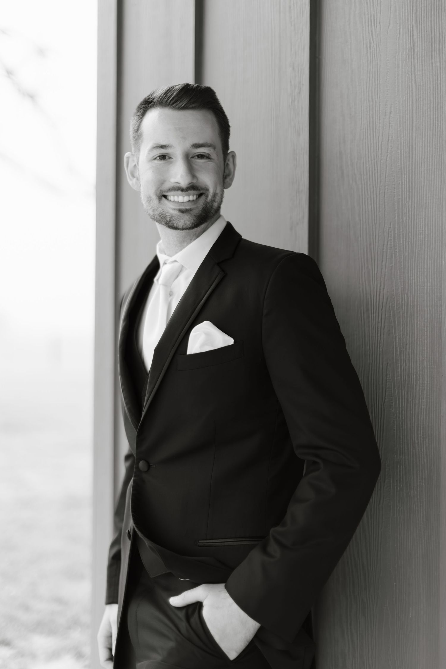 Black and white portrait of a person in a formal suit smiling against a light background.