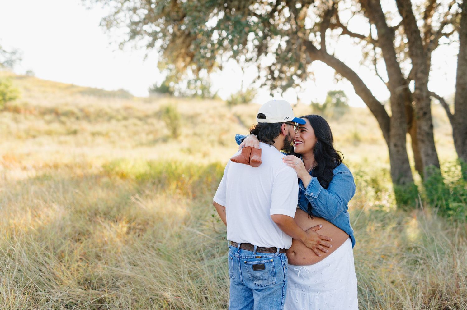 A couple embraces in a romantic outdoor photoshoot among trees and golden sunlight.