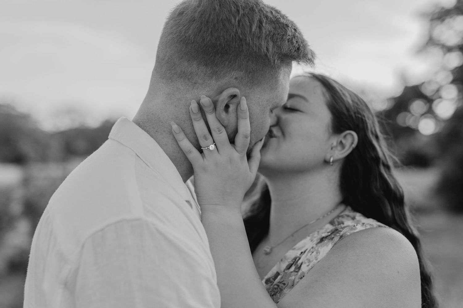 A romantic black and white portrait of a couple sharing a tender kiss outdoors.