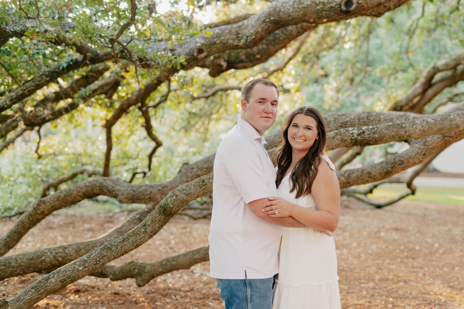 A couple poses together against the backdrop of a majestic oak tree.