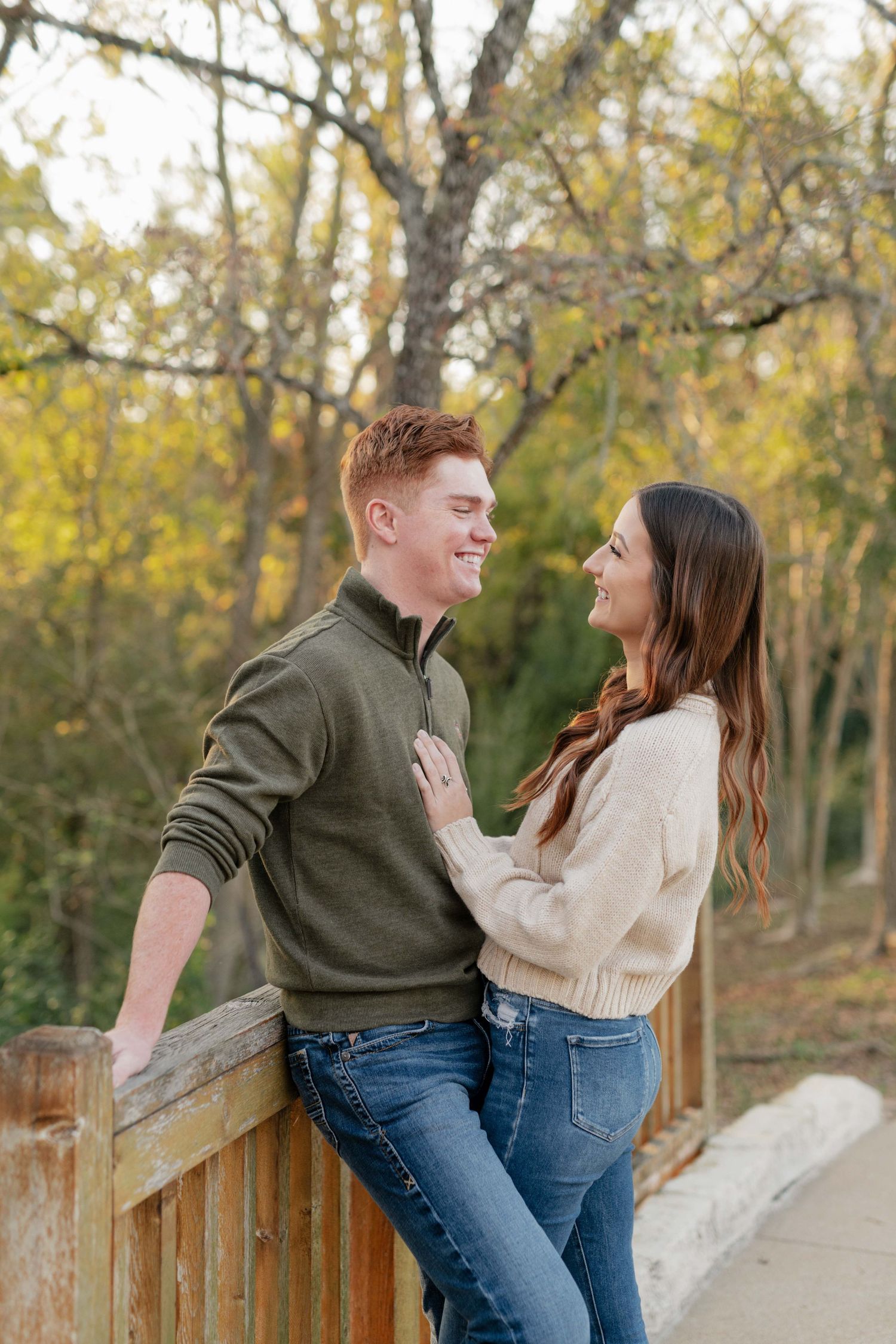 Couple shares a romantic moment on a wooden bridge with fall foliage in background.