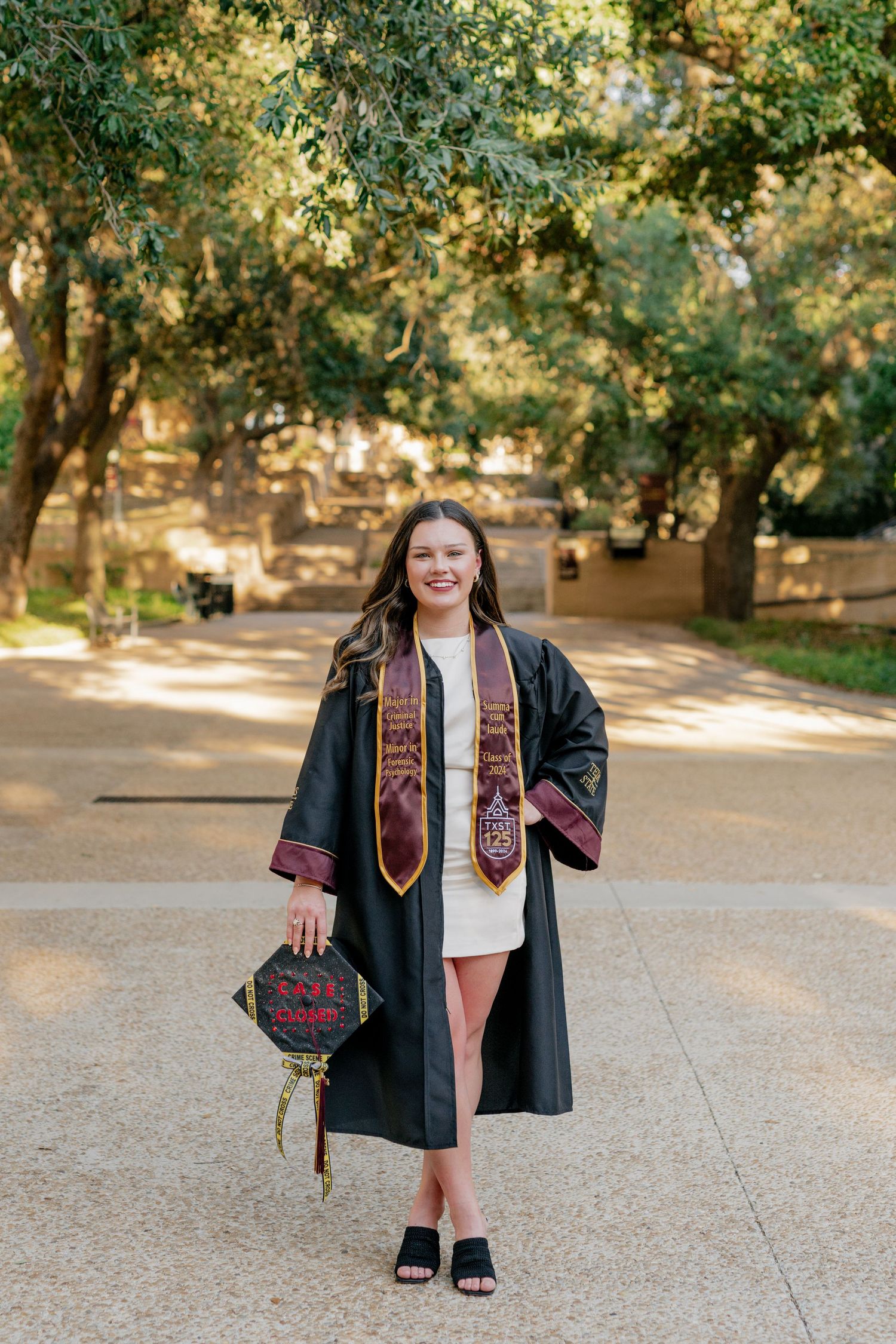 Senior session at Texas State University. The senior poses underneath the tree canopy on a walkway.