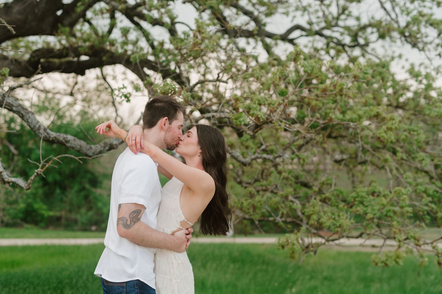 Romantic couple embraces under blooming spring trees in an outdoor garden setting during golden hour.