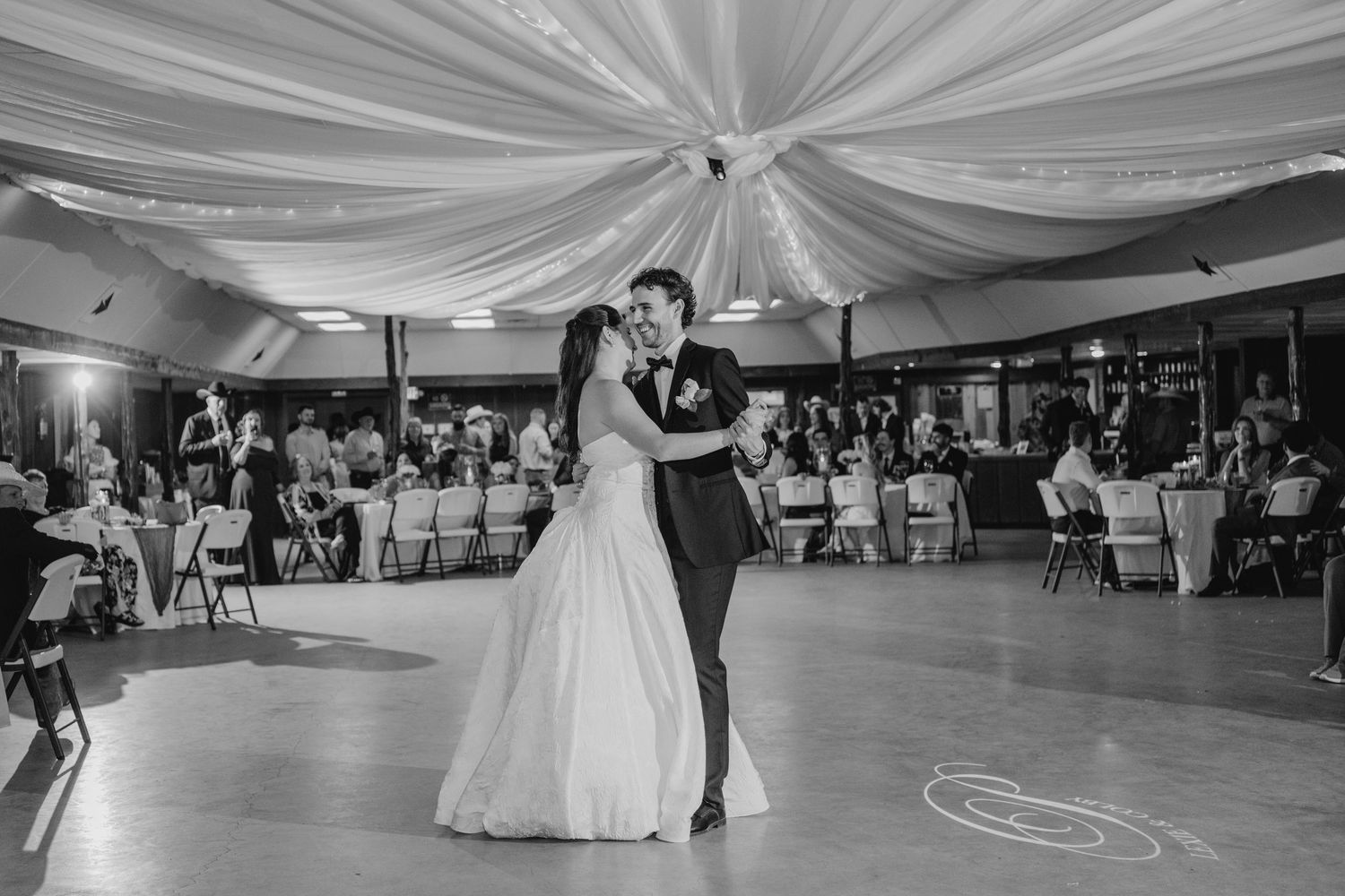 Bride and groom share first dance in black and white photo at elegant wedding reception.