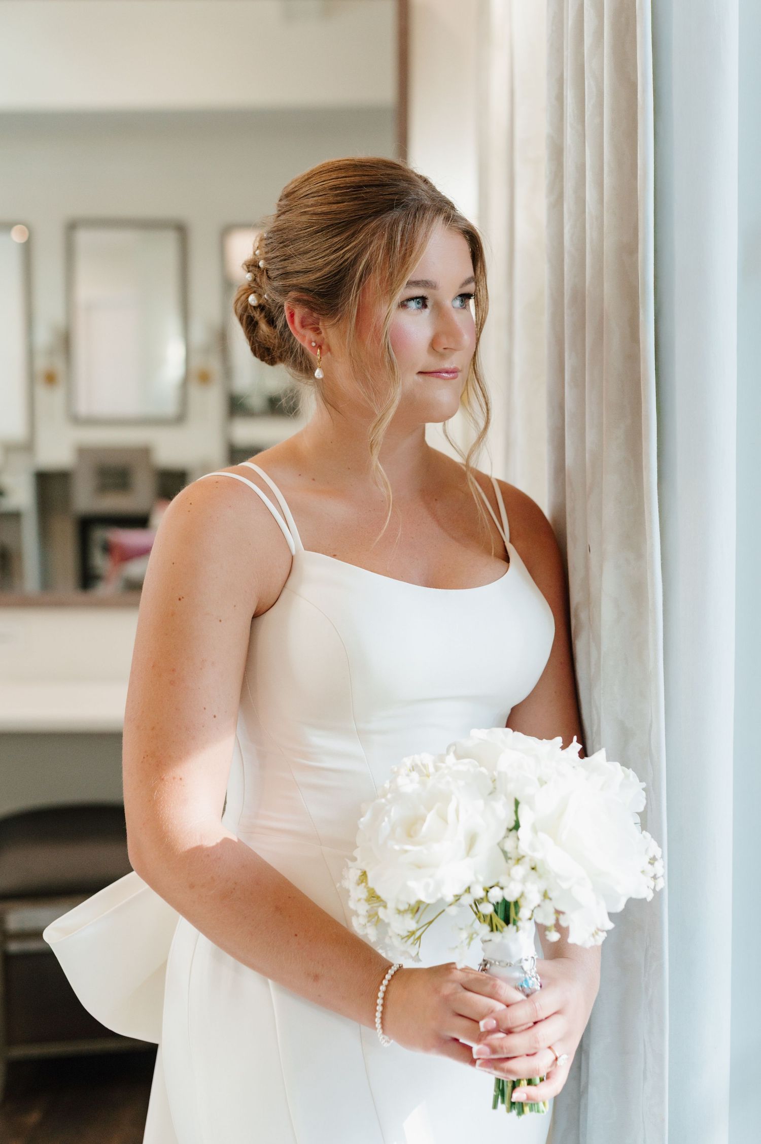 A bride in a white wedding dress holds a bouquet of white flowers while posing indoors.