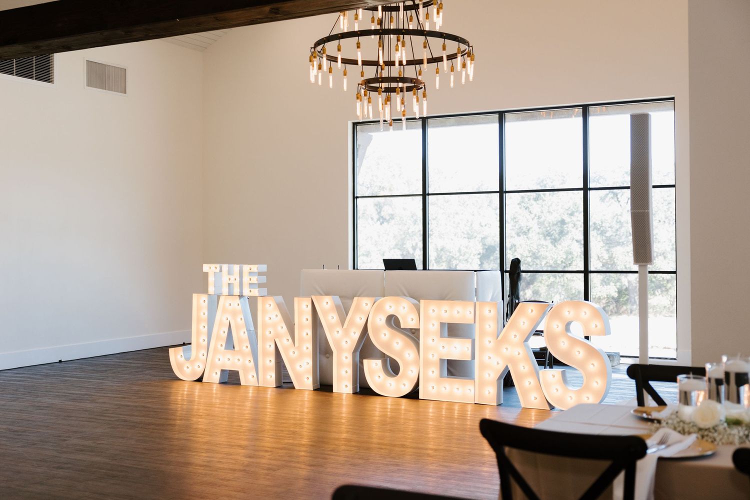 Large illuminated white letters spell out text against a white wall in a modern event space with chandeliers.