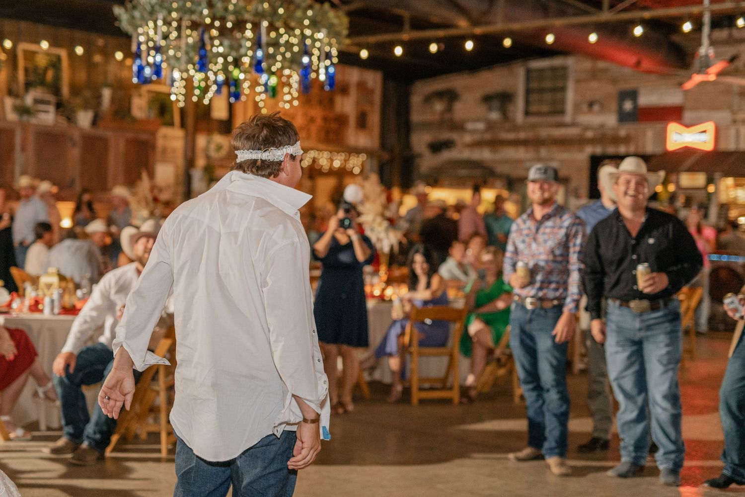 Reception guests dance and celebrate under string lights in a country-style barn venue.