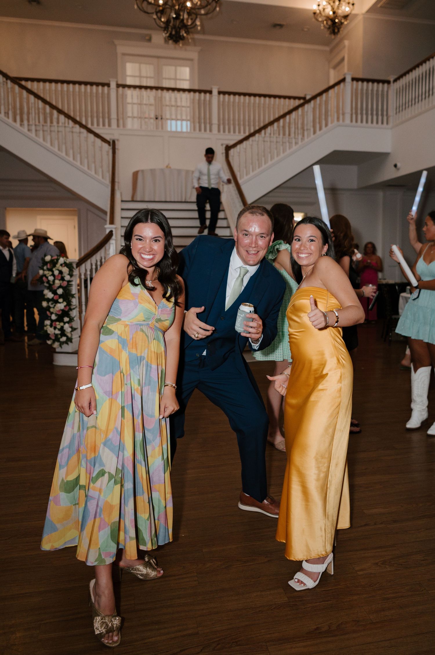 Wedding reception guests dancing and celebrating on a wooden dance floor under chandeliers.