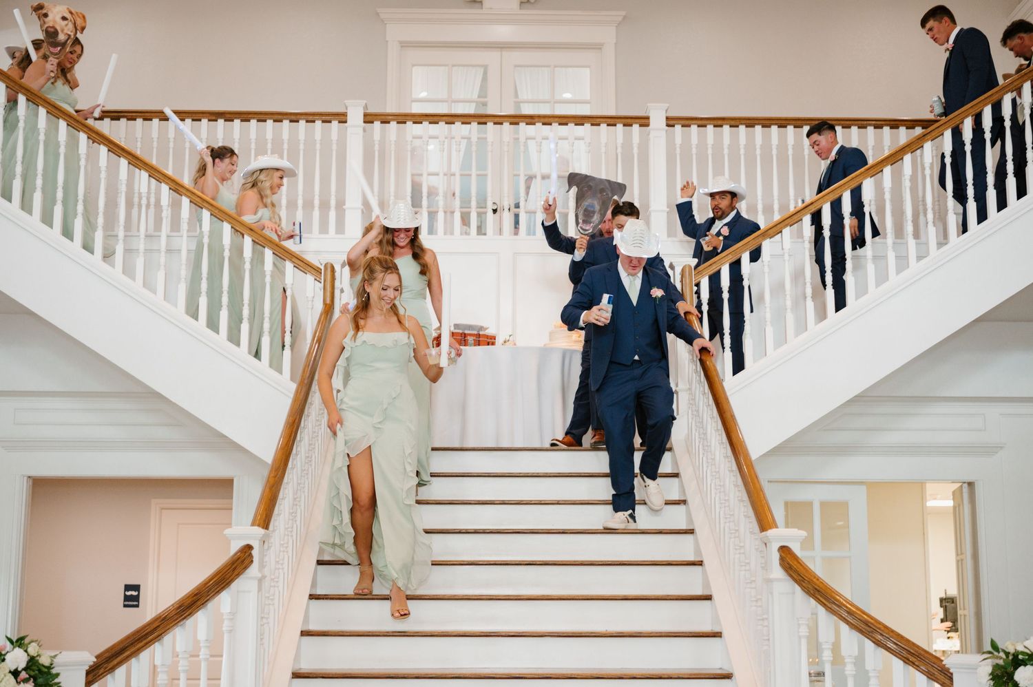 Newlyweds descending a grand white staircase in playful poses during their wedding celebration.