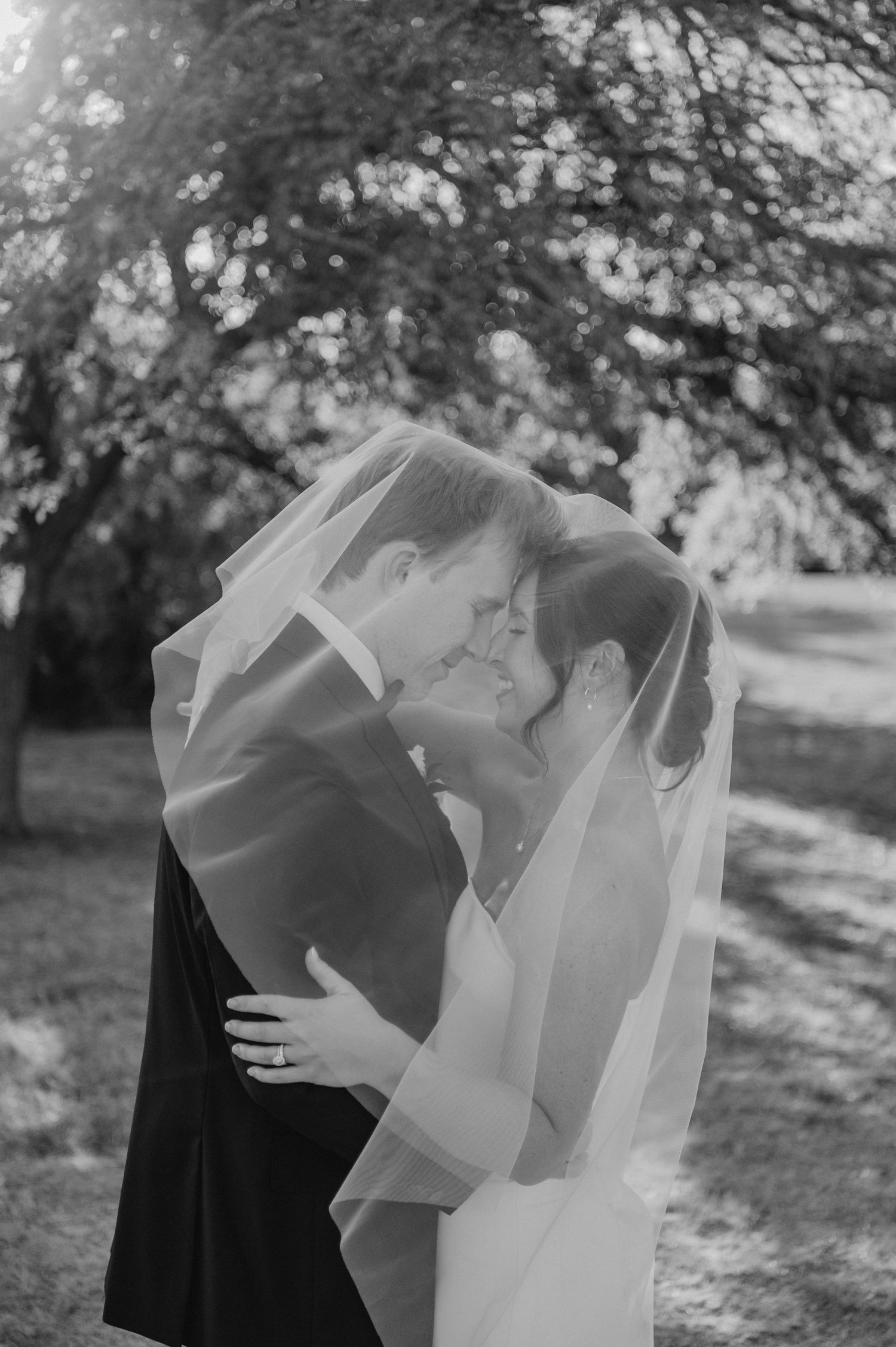 A romantic black and white photo sequence showing a couple in wedding attire sharing intimate moments under tree branches.