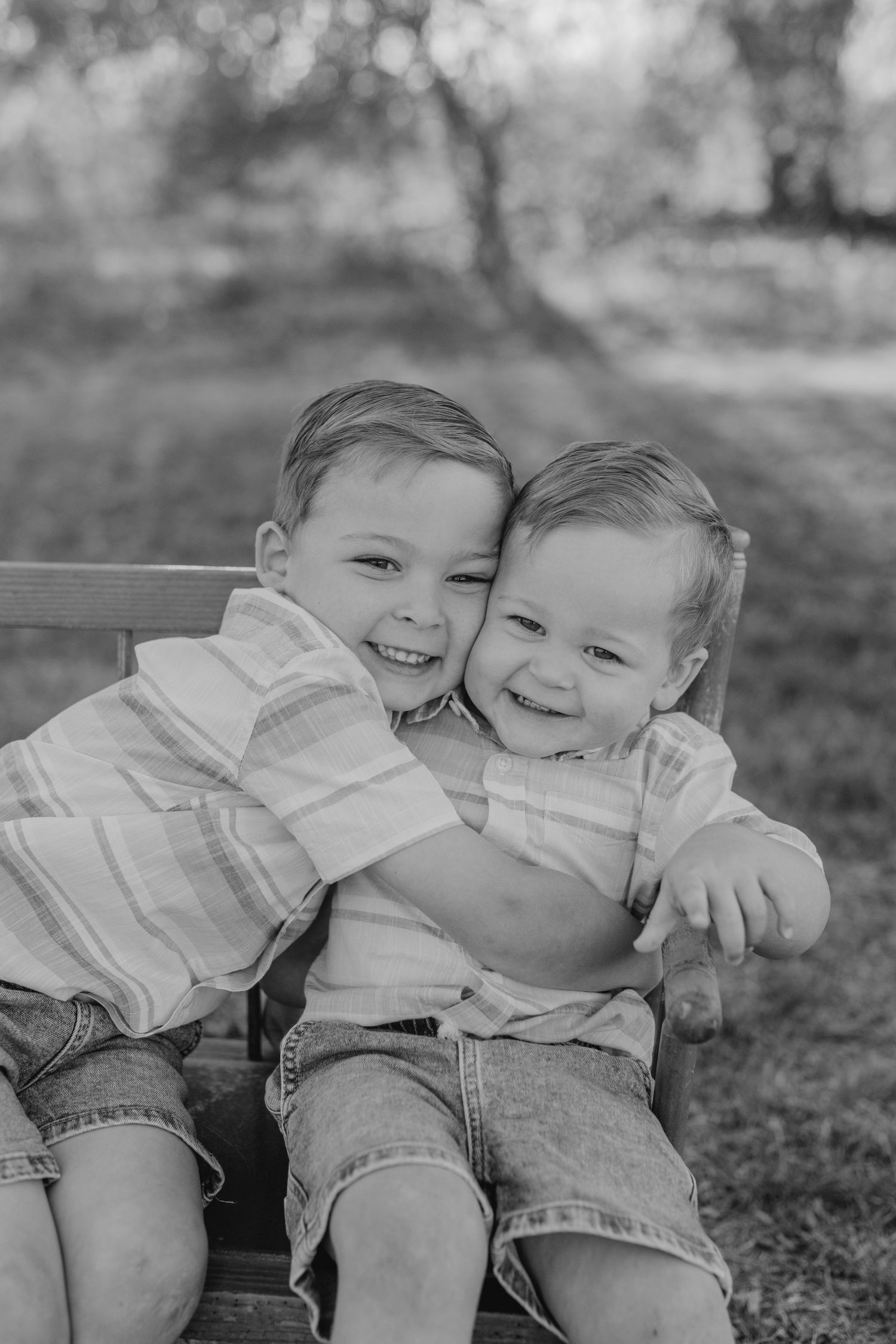 Two young children sit close together on a bench outdoors, sharing a sweet moment in black and white.