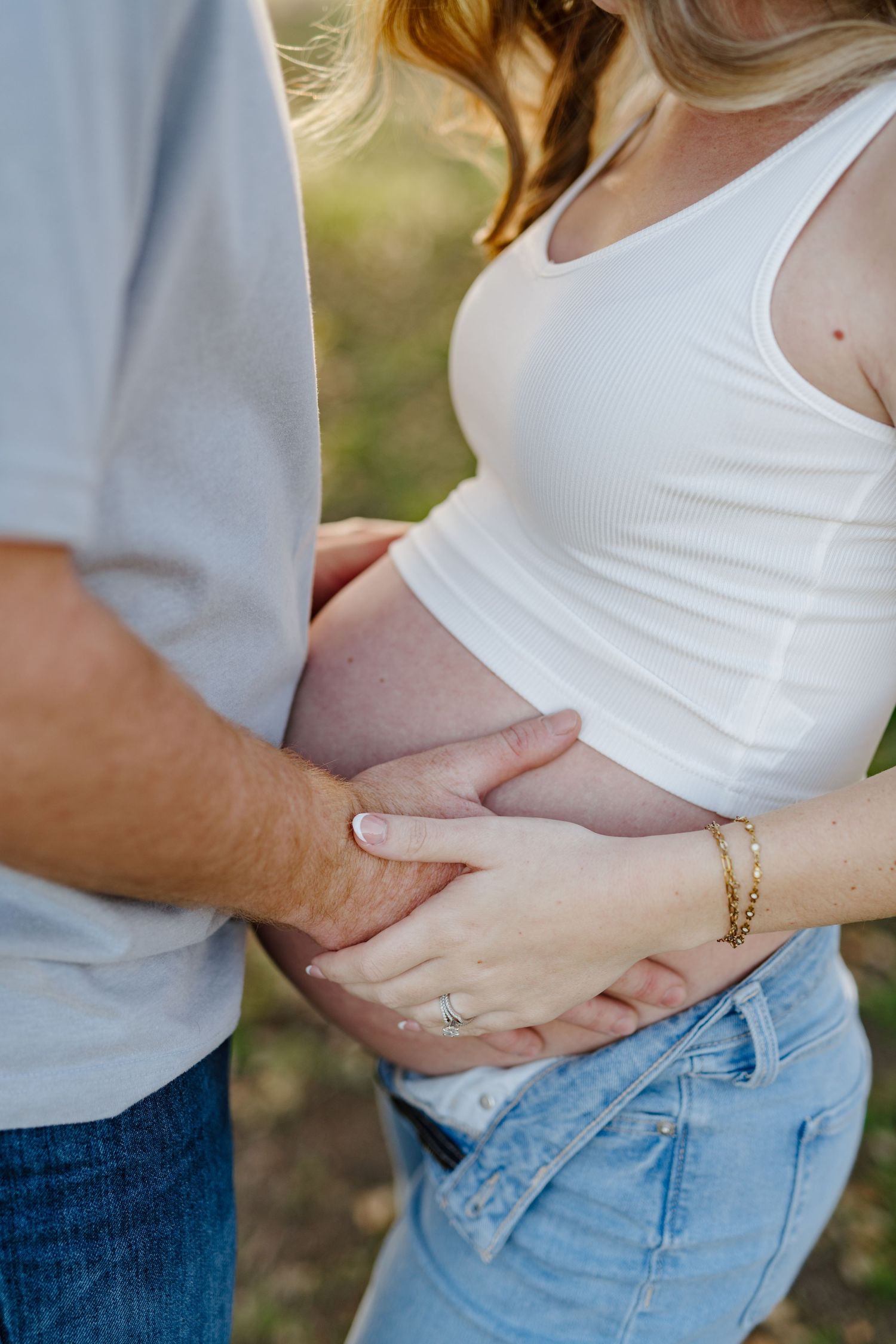 Close-up shot of hands tenderly cradling a pregnant belly against a soft natural backdrop.