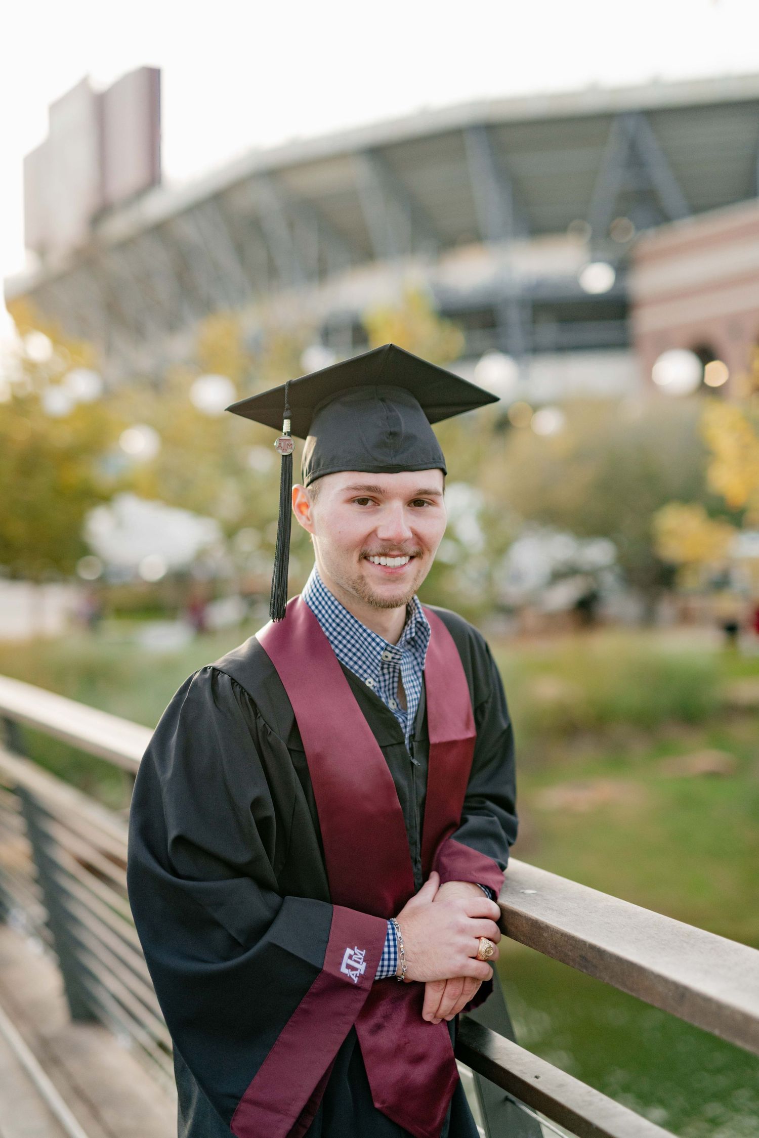 Graduate in cap and gown poses near stadium with maroon stole.