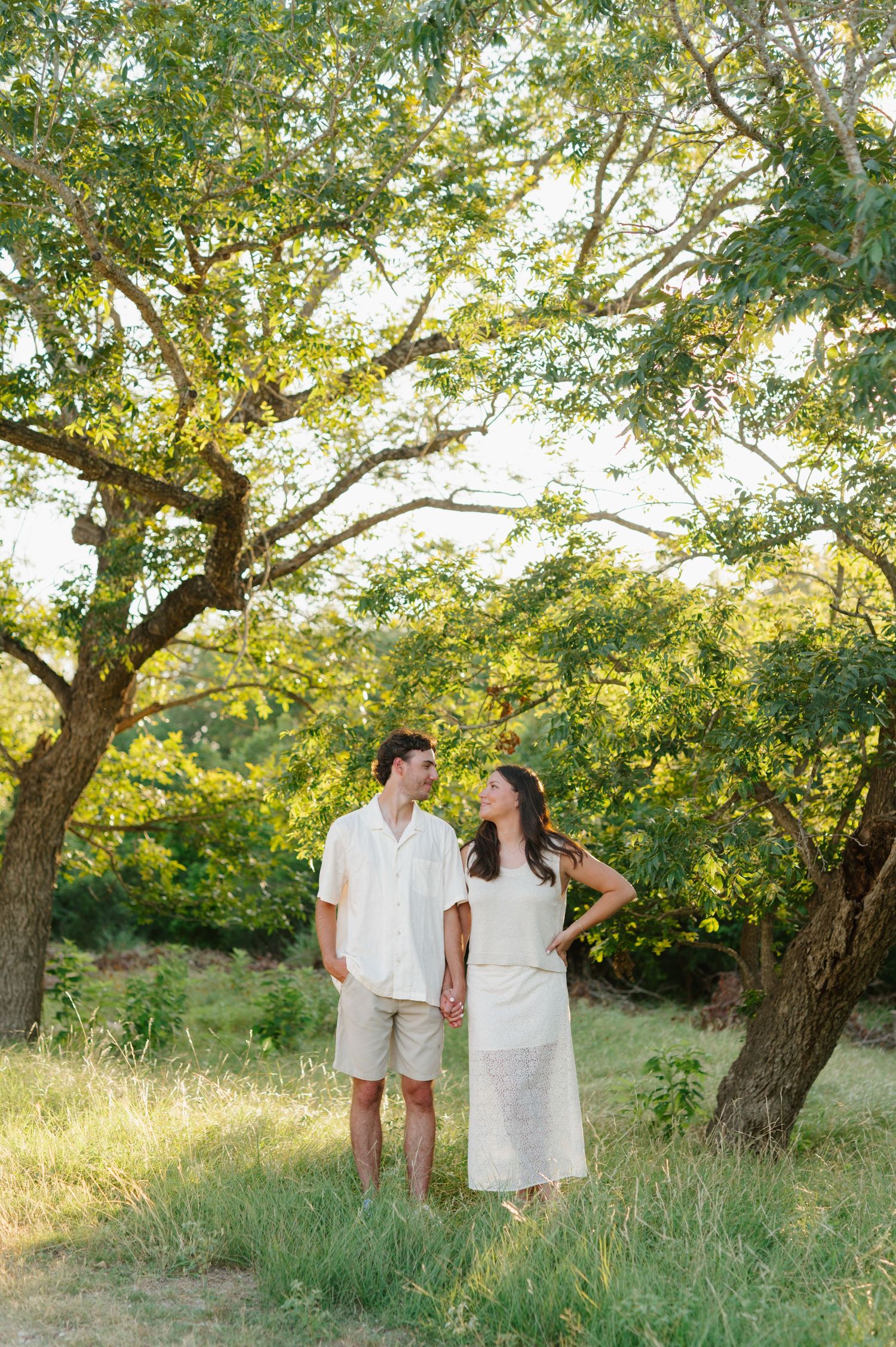 A couple walking together under beautiful green trees during a summer photo session.