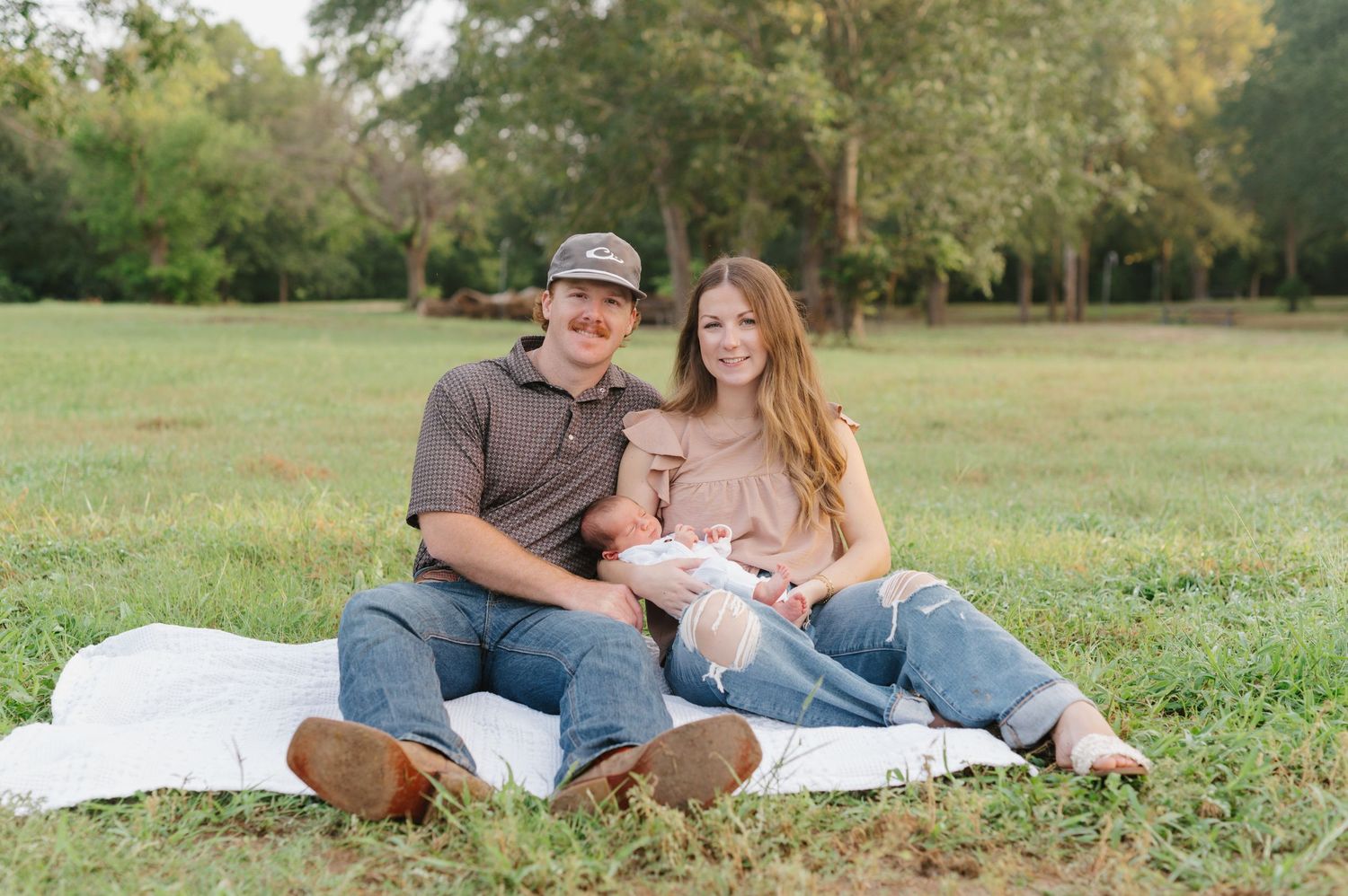 Family relaxes together on white blanket in grassy field during outdoor photo session.