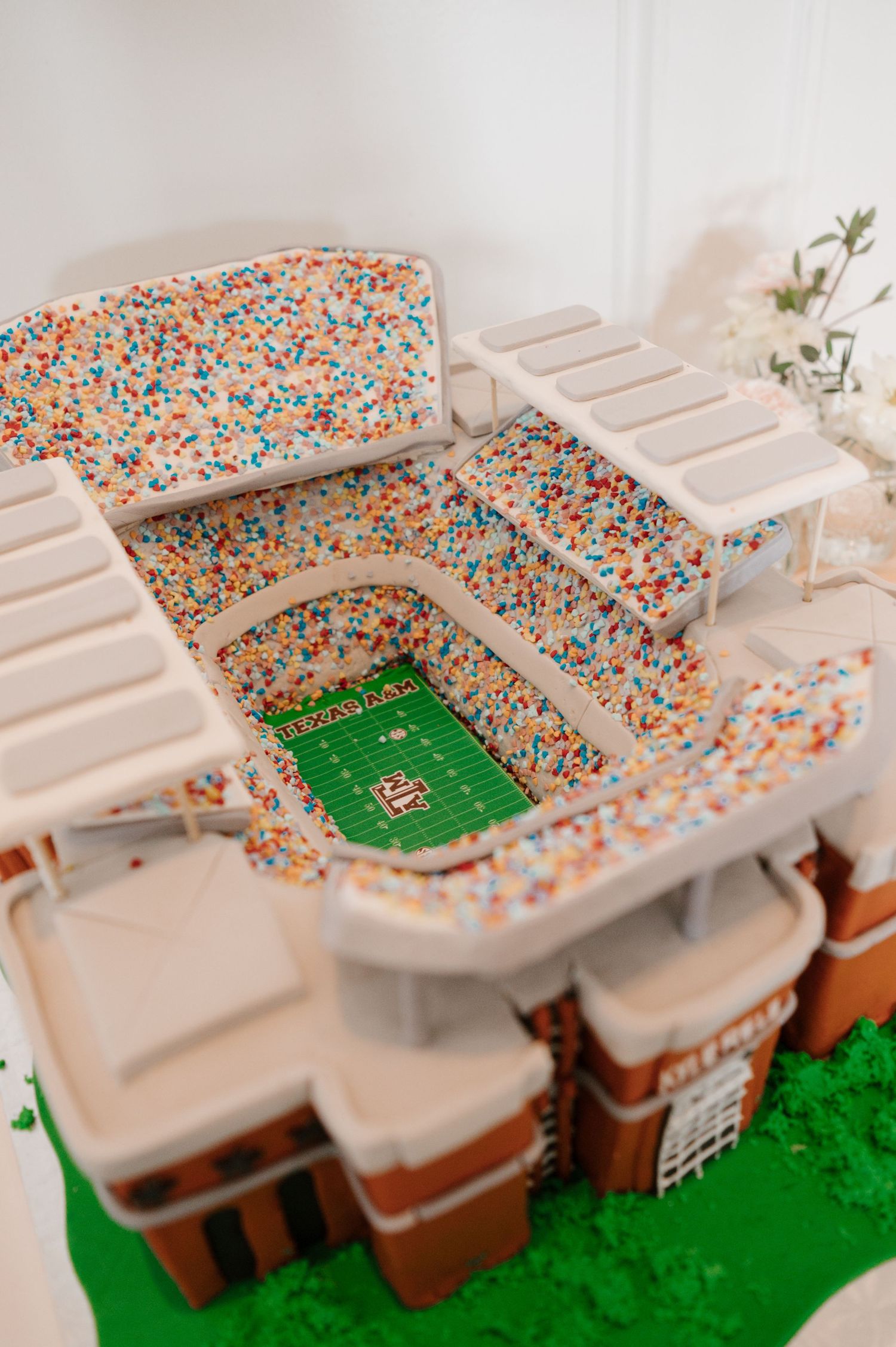 Stadium-shaped wedding cake display with intricate confetti details and football field design.