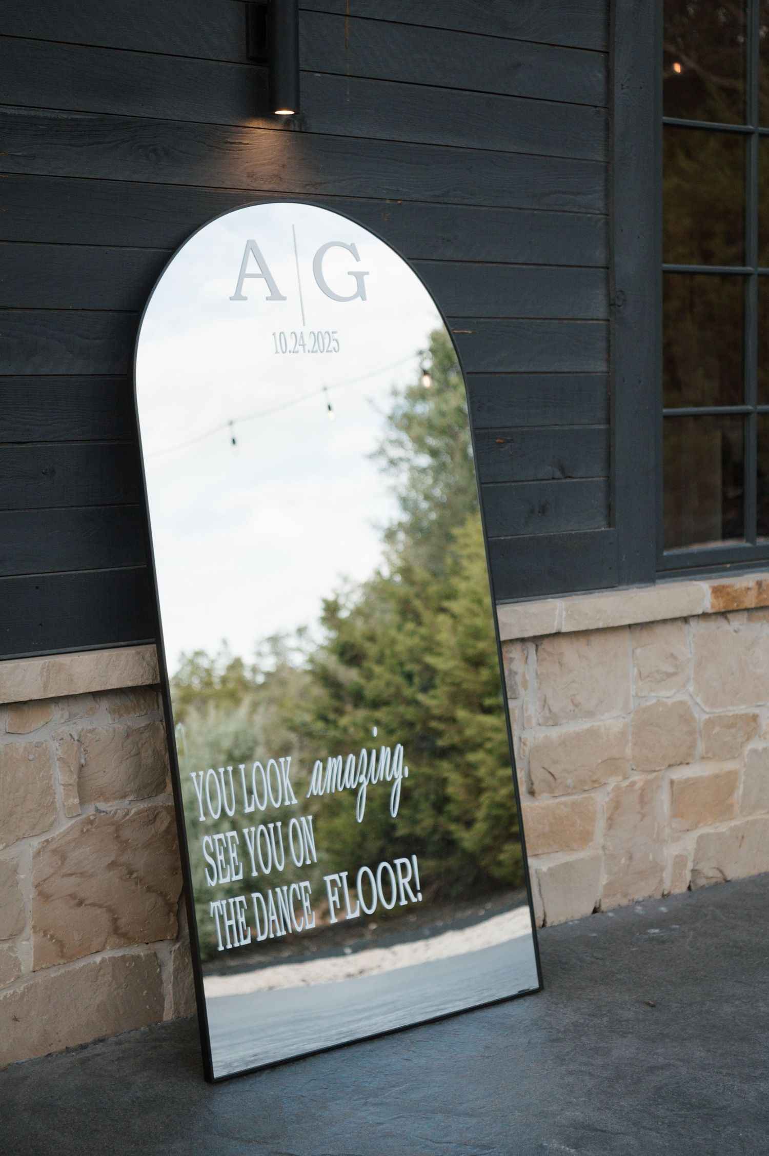 A large mirror with the letters 'AG' reflected in it, showing the outdoor scenery behind it.