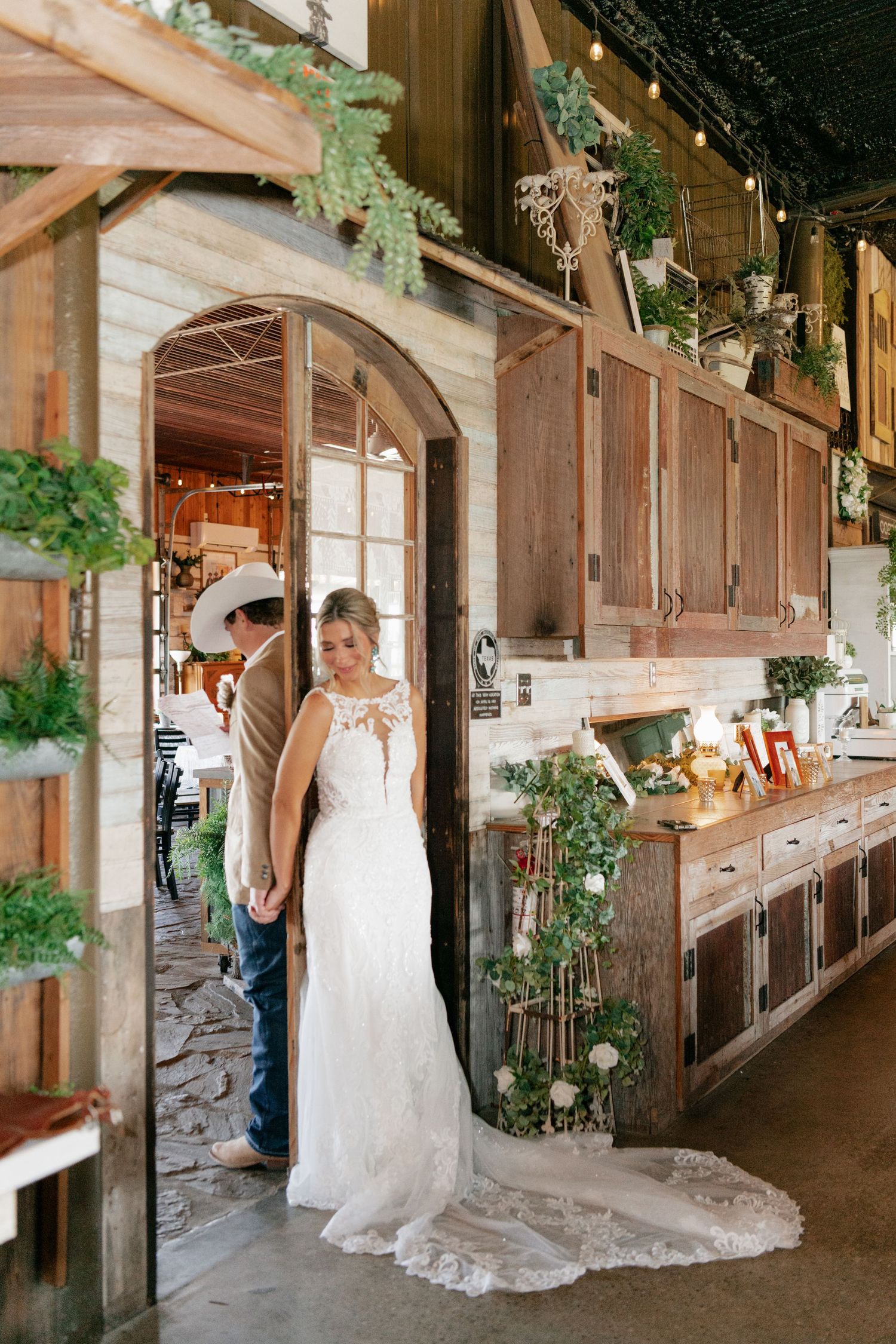 A couple share an intimate first look moment in a rustic wooden barn decorated with greenery.