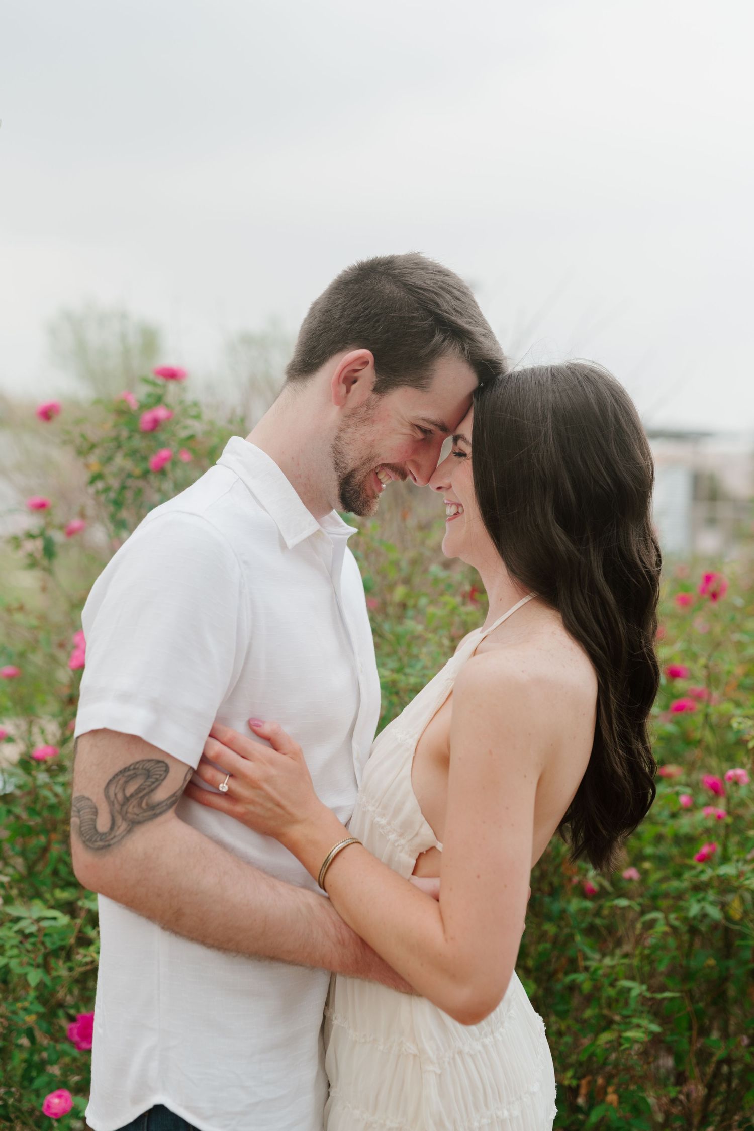 A couple shares an intimate moment together in a garden filled with blooming red roses on a misty day.