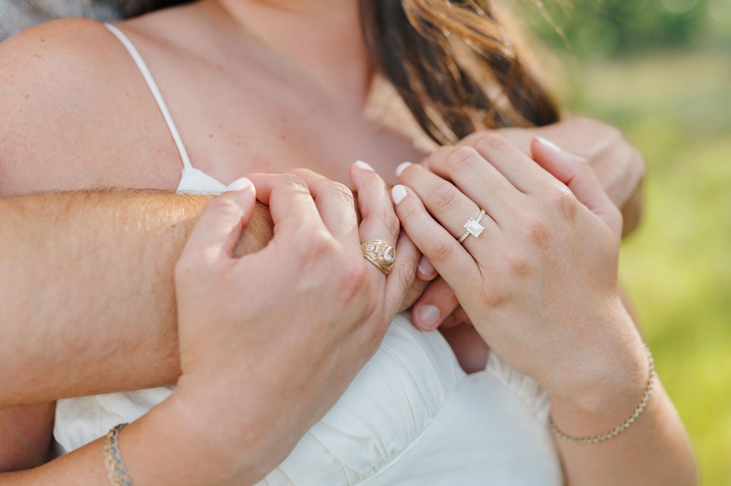 Hands holding and exchanging wedding rings outdoors against a soft green natural background.
