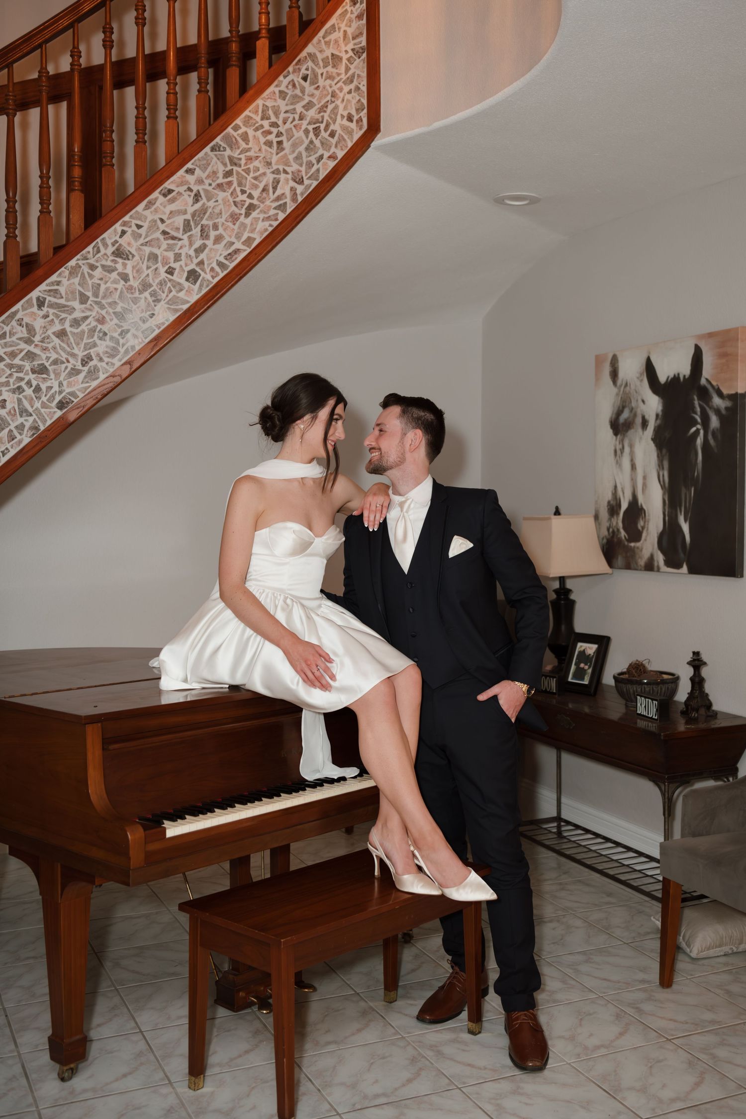 Playful couple interacting near a wooden piano during their wedding celebration.