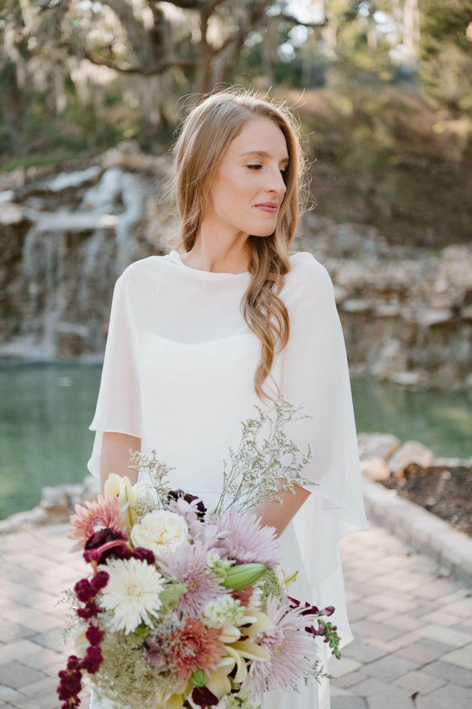 An elegant bridal bouquet with burgundy dahlias and pink chrysanthemums against a natural outdoor backdrop.