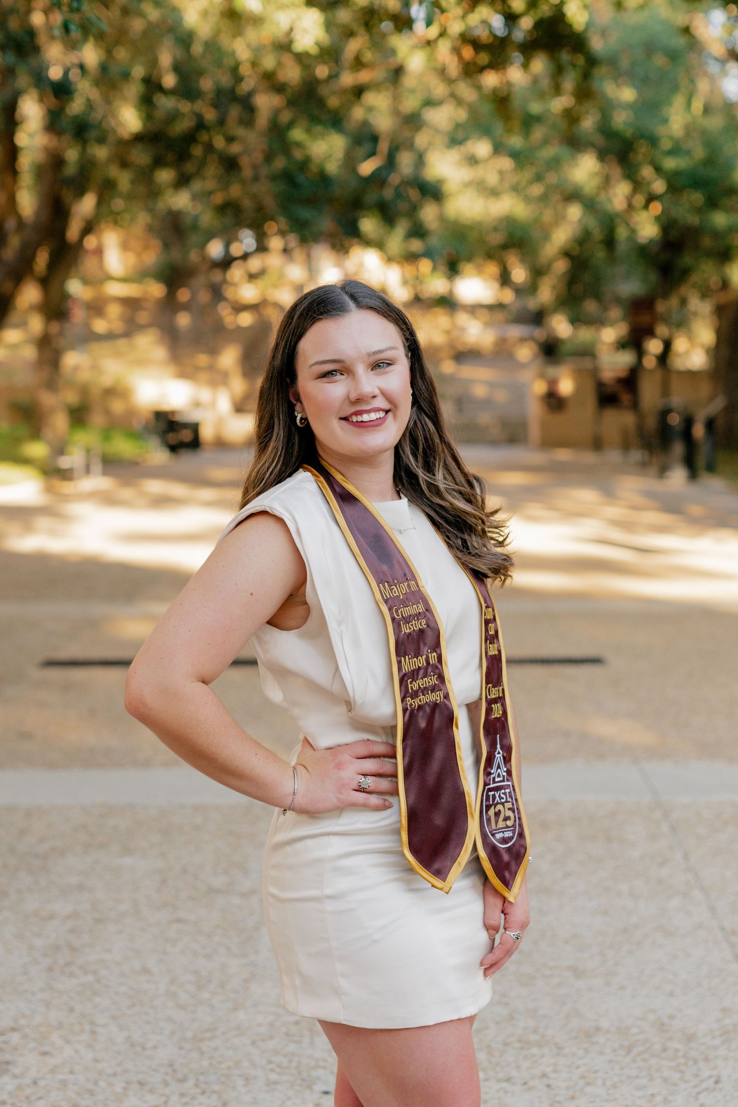 Senior session at Texas State University. The senior poses underneath the tree canopy on a walkway.